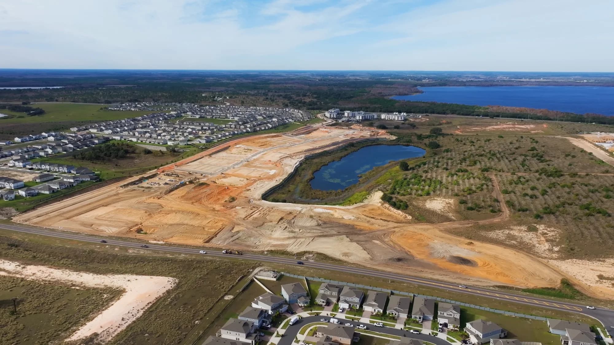 Aerial of a community under construction beside a retention pond, with the first finished homes alongside