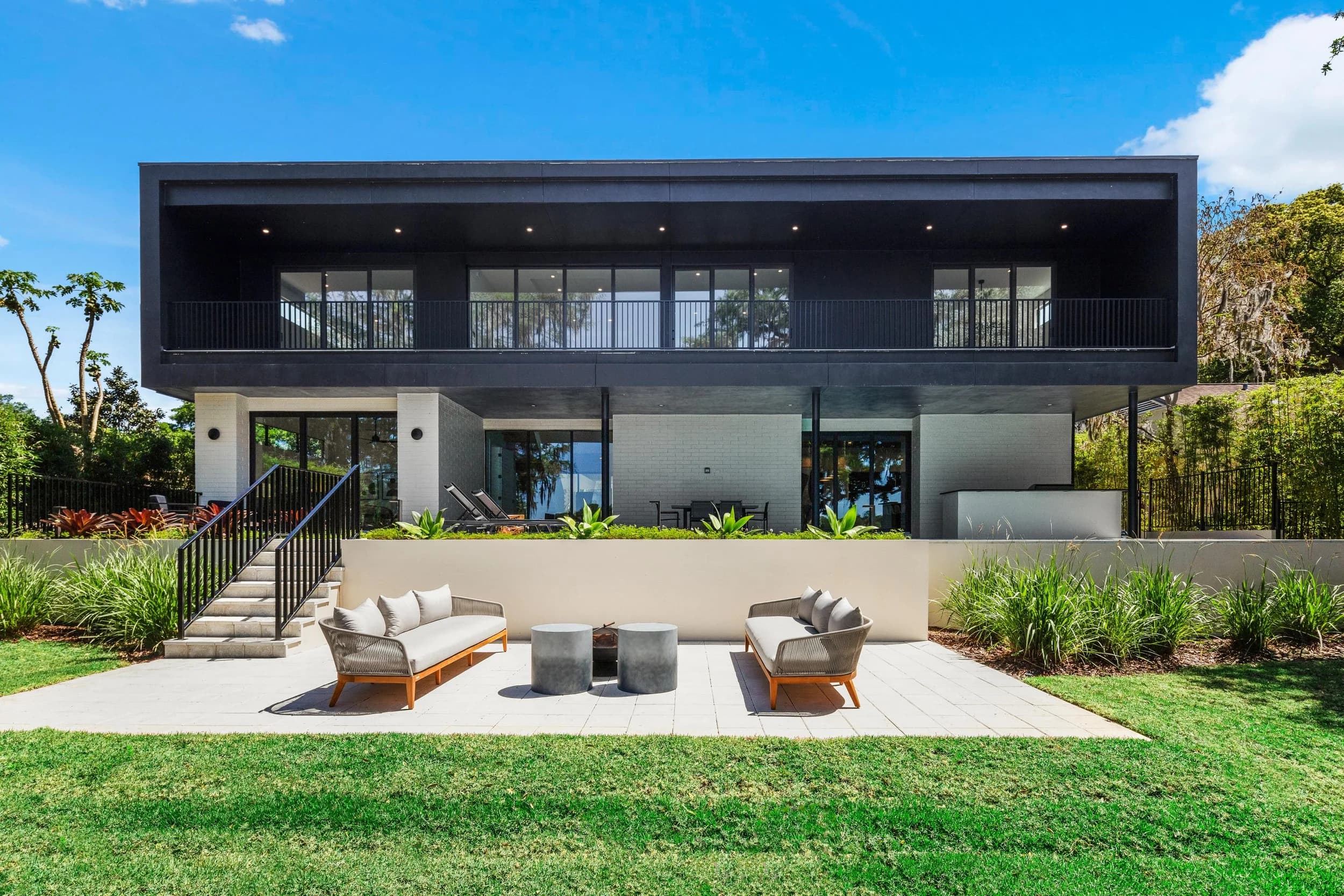 Modern black two-story home rear elevation with patio seating