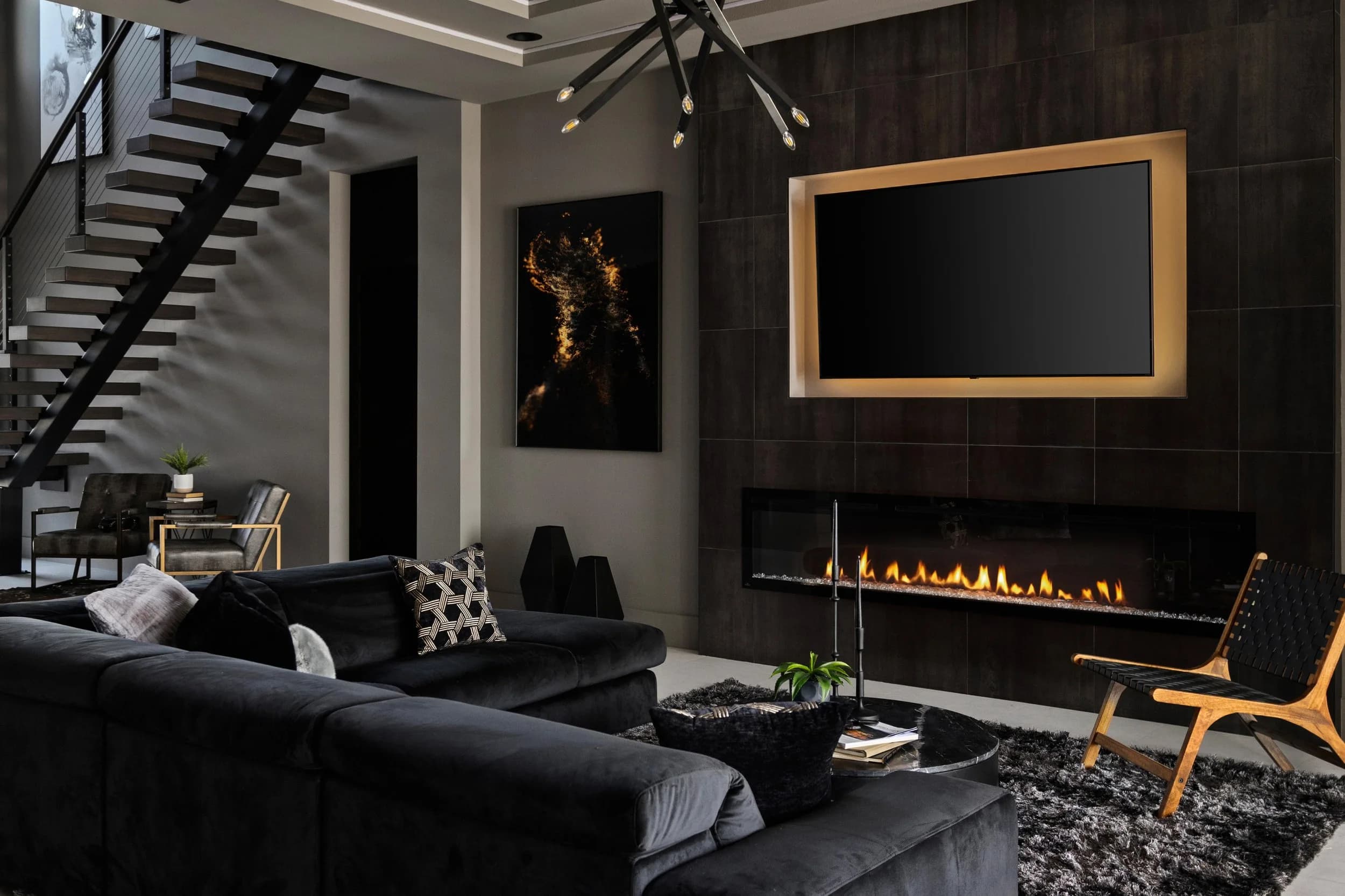 Model home great room with black sectional, linear fireplace, and floating stair