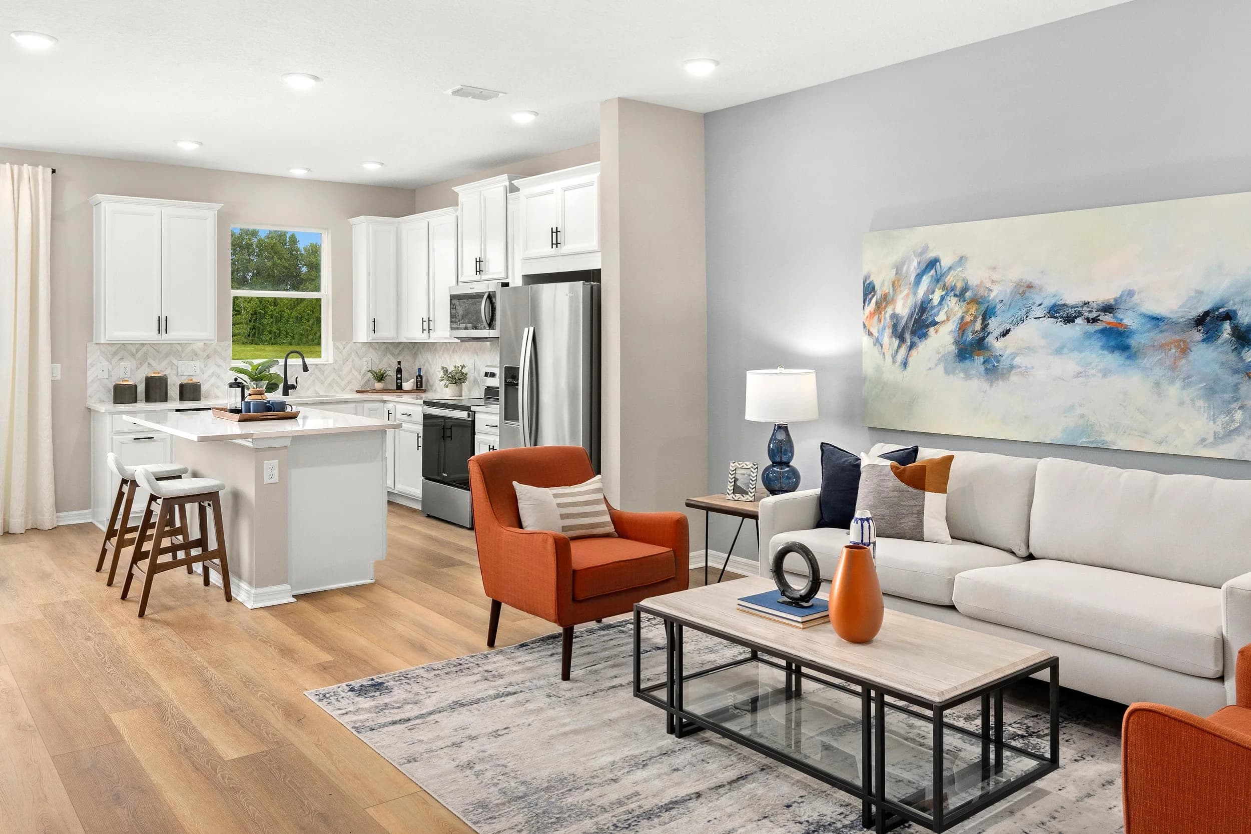 Bright model home kitchen and living room with white cabinetry and an orange armchair