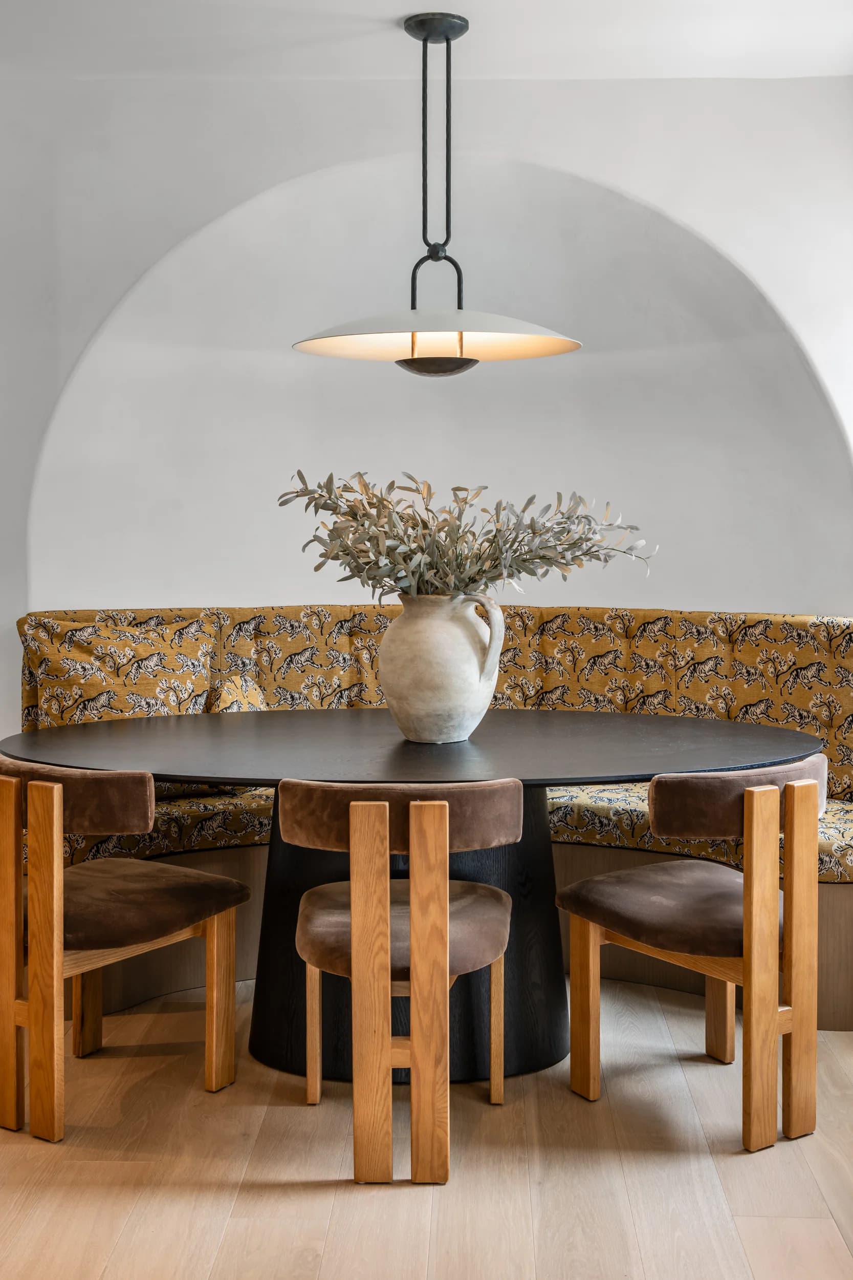 Dining nook with a black round table, leather chairs, and a patterned banquette set into a plaster arch