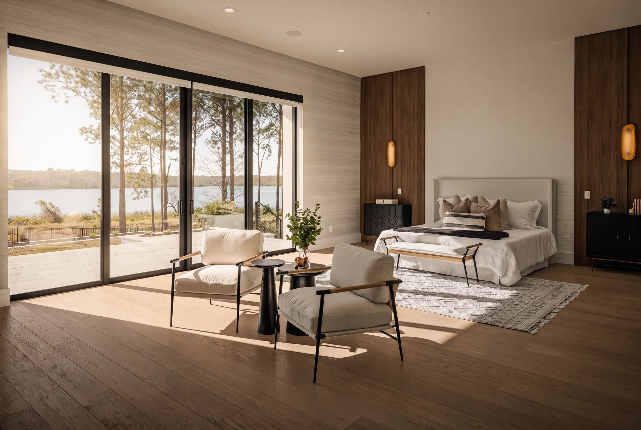 Primary bedroom with floor-to-ceiling sliding glass to a lake view, walnut feature wall, and a sitting area with sculptural chairs