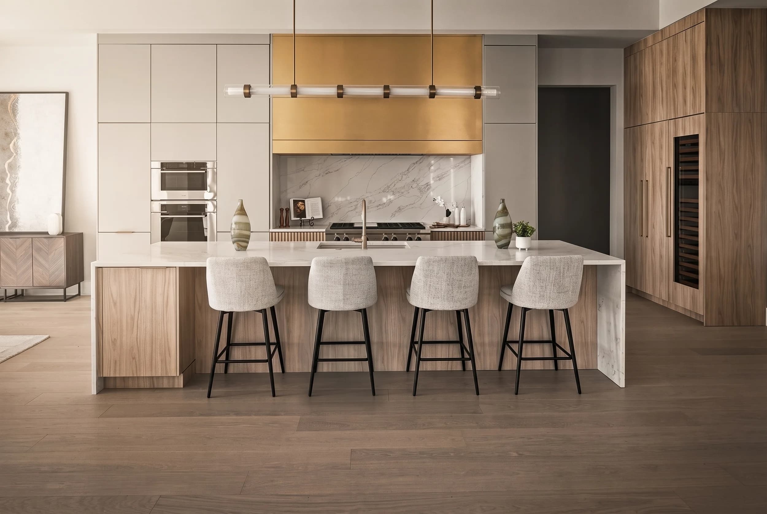 Modern kitchen with white oak cabinetry, brass range hood, waterfall marble island, and upholstered counter stools