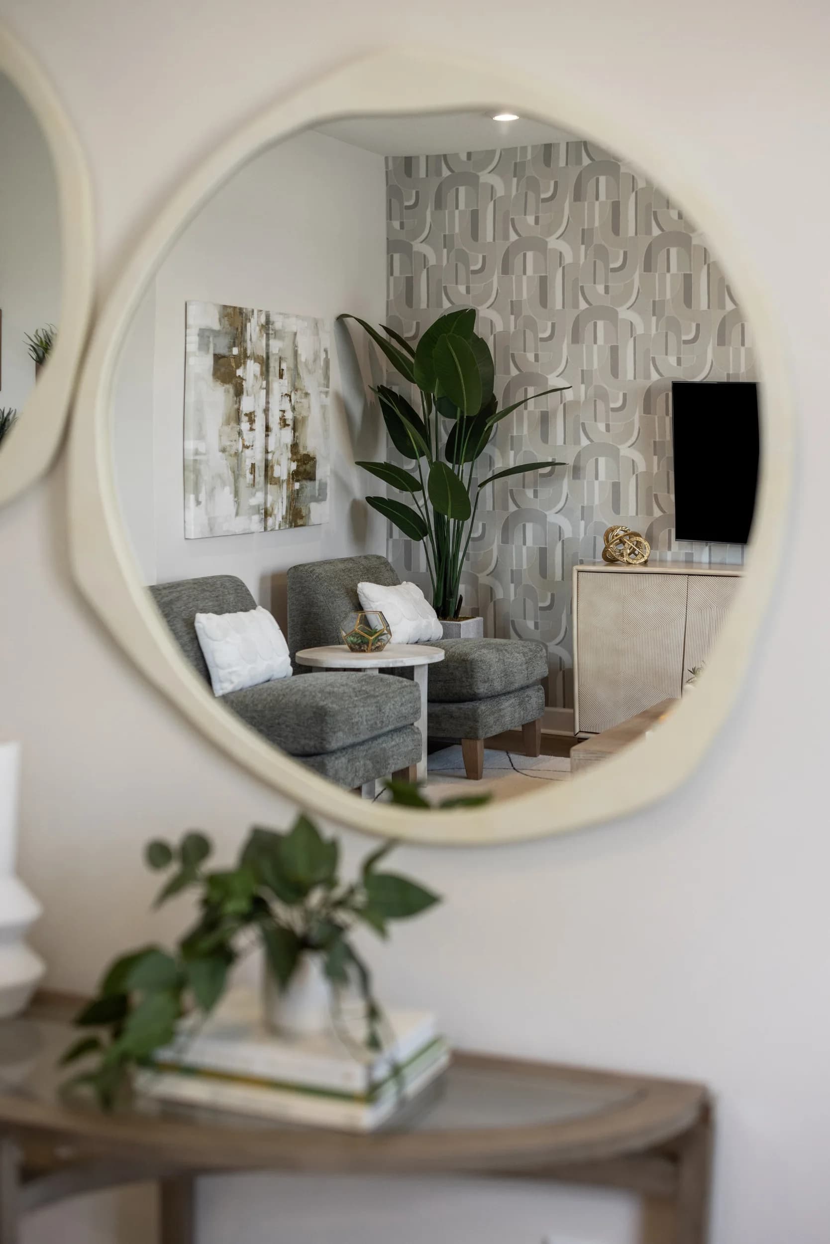 Round mirror reflecting a styled sitting area in a model home entry