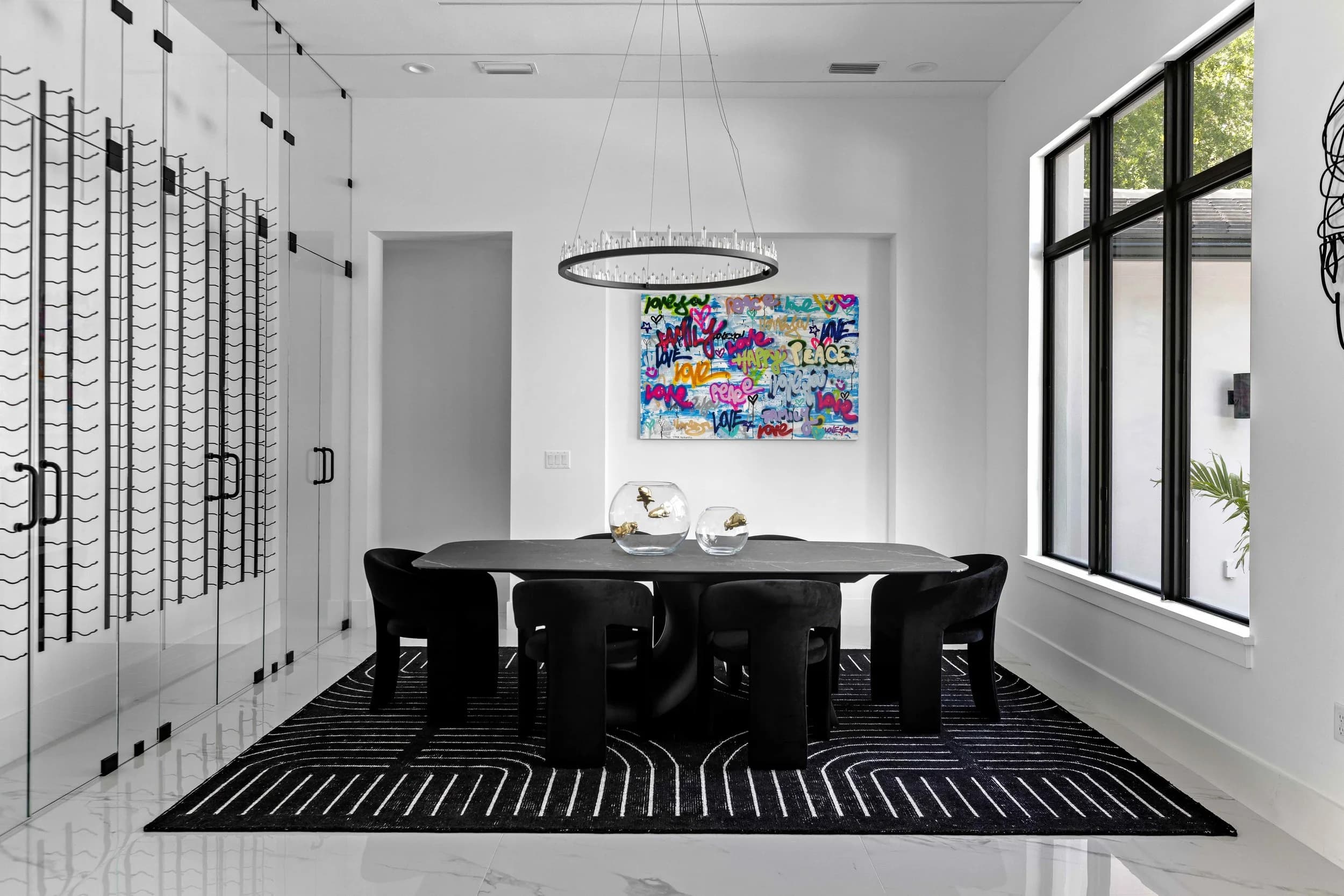Dining room with glass wine wall, black velvet chairs, and a ring chandelier