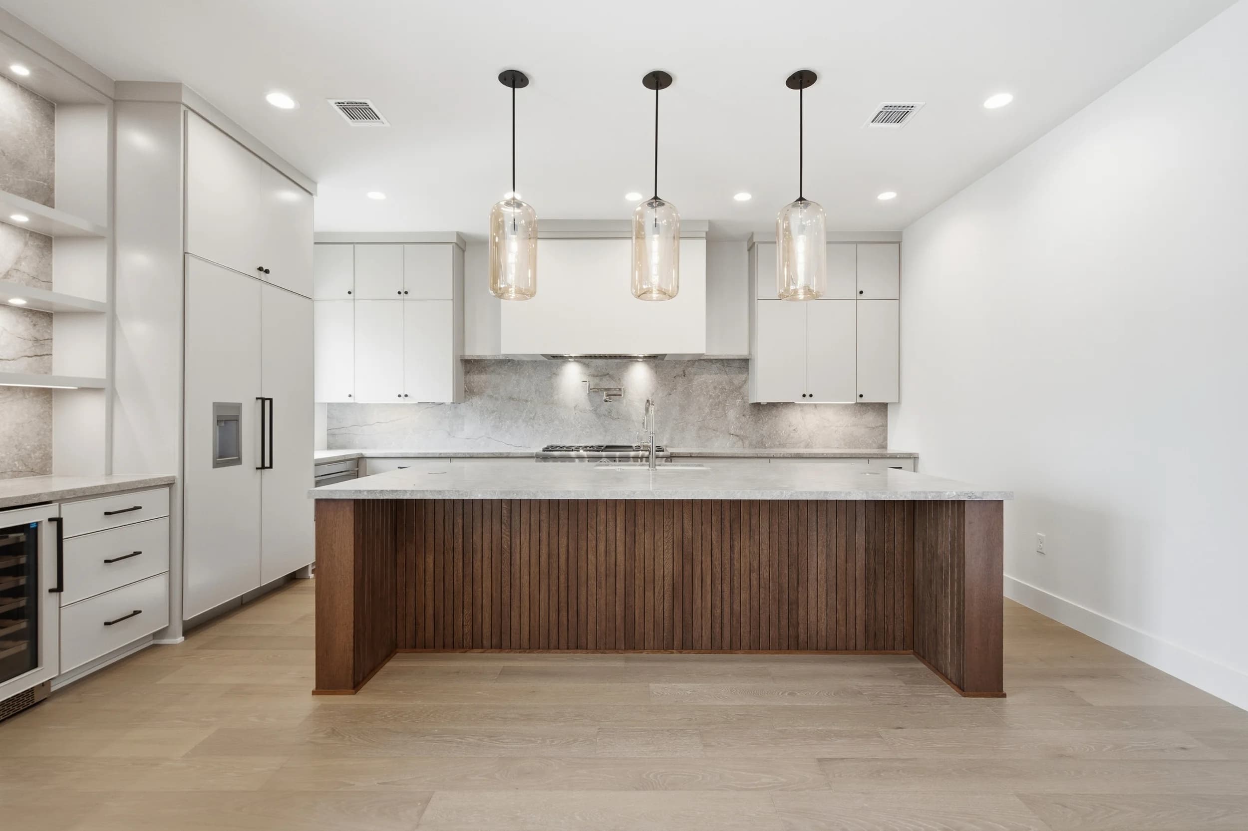 Kitchen with a fluted walnut island, quartzite counters and three glass pendants