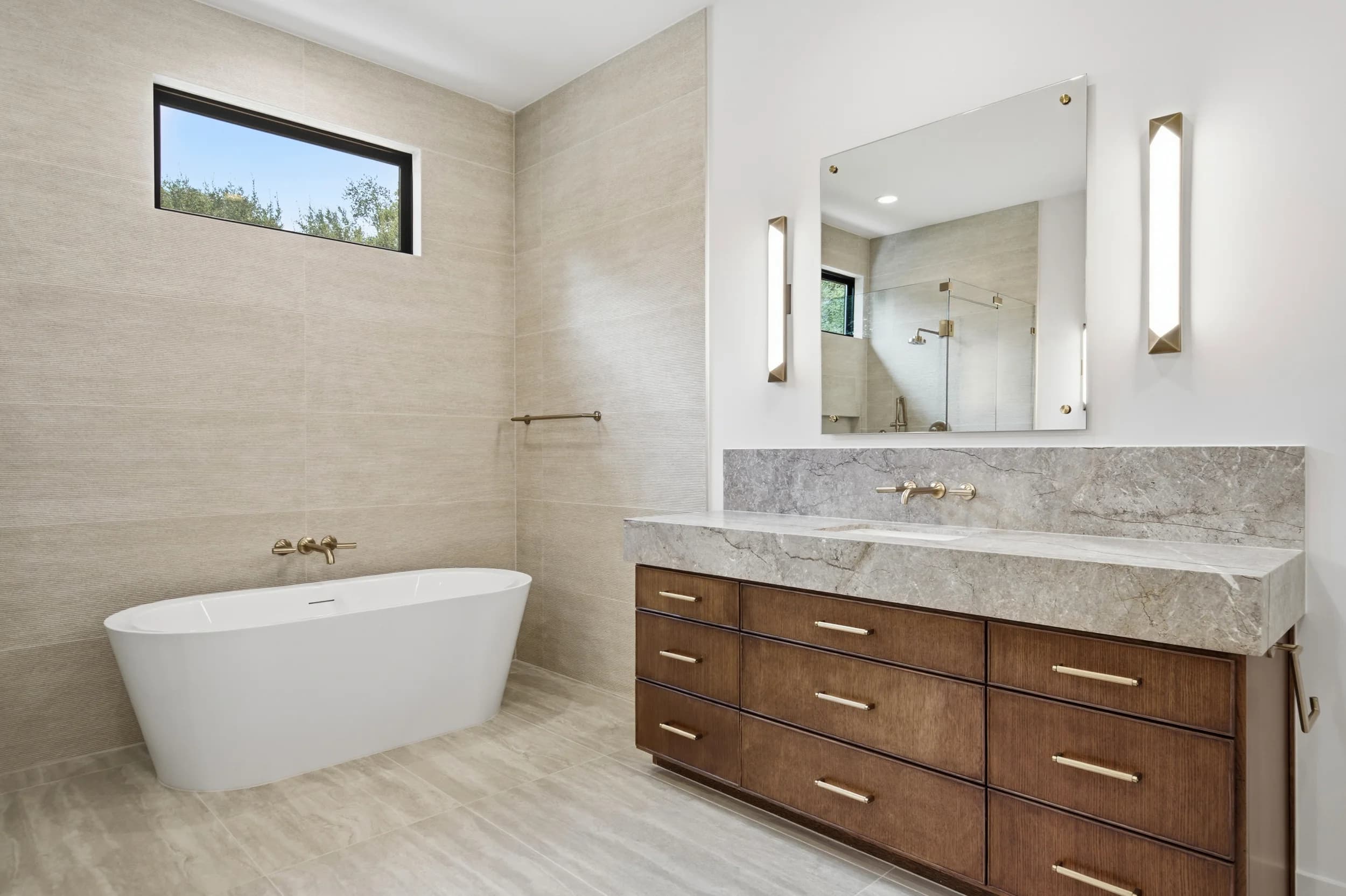 Primary bath with a freestanding tub, walnut vanity and stone counters