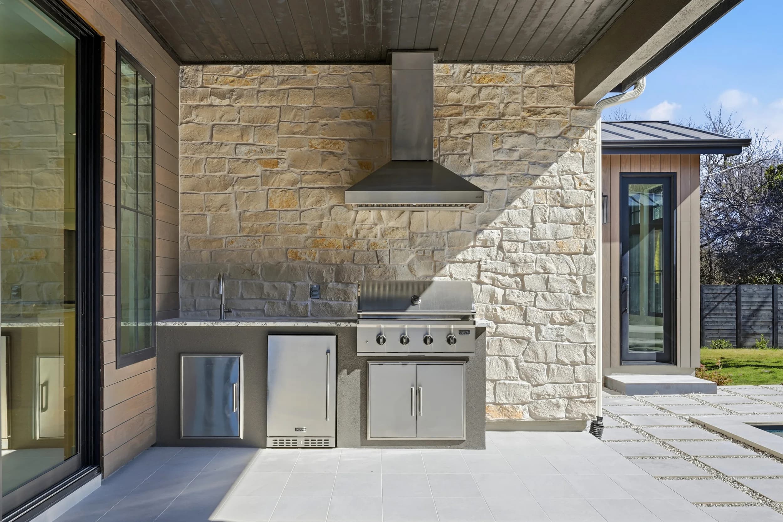 Covered outdoor kitchen with a stone wall, stainless grill and vent hood