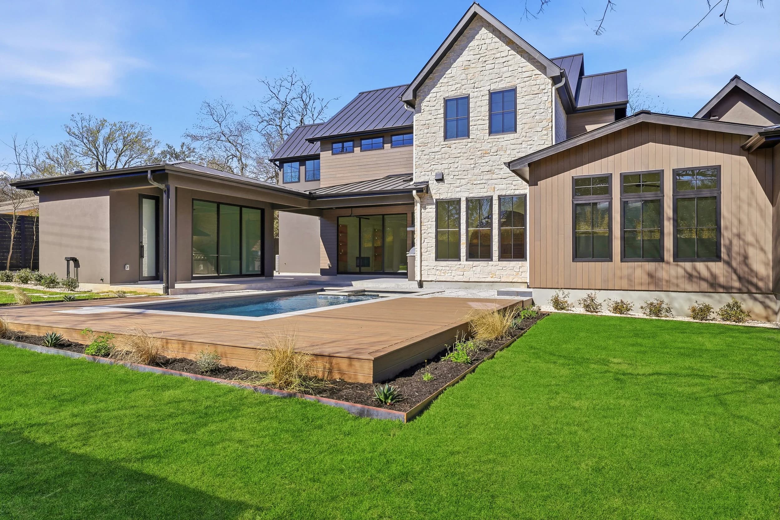 Rear of a limestone and wood-clad home with a pool set into a raised deck
