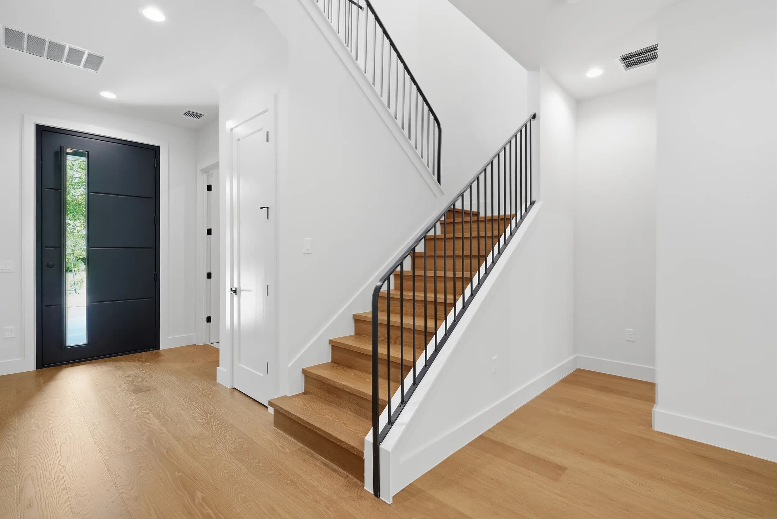 Entry with a black pivot door and an oak staircase with a black metal railing
