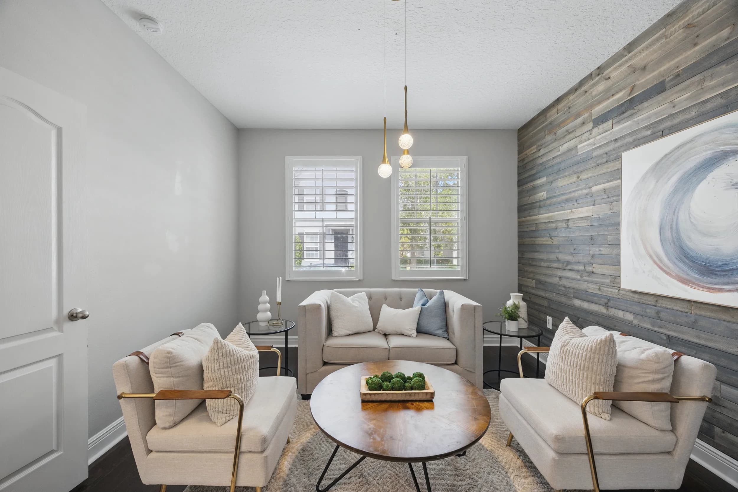 Staged living room with cream loveseat and accent chairs, round wood coffee table, and a reclaimed-wood accent wall