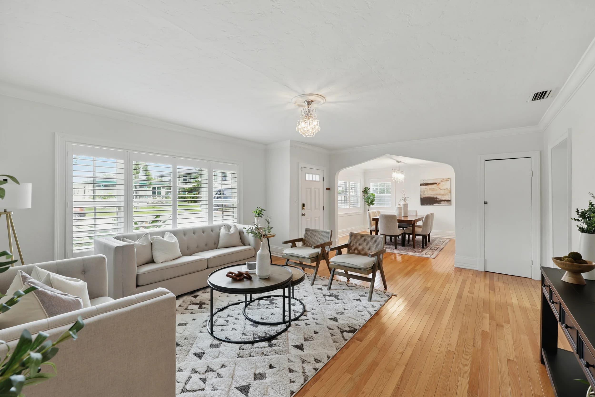 Living room with oak floors, plantation shutters, linen sectional and geometric rug, arch to dining room