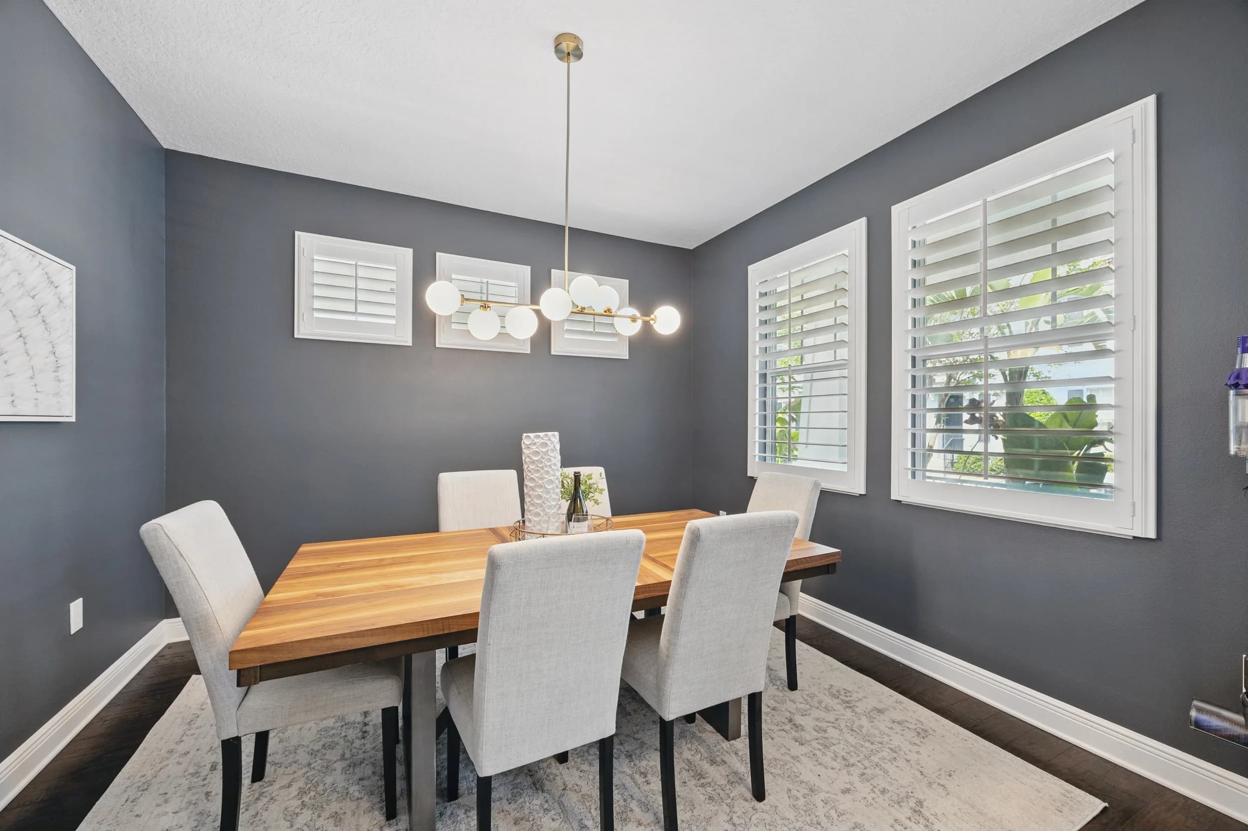 Charcoal-walled dining room with wood table, upholstered chairs and brass globe chandelier