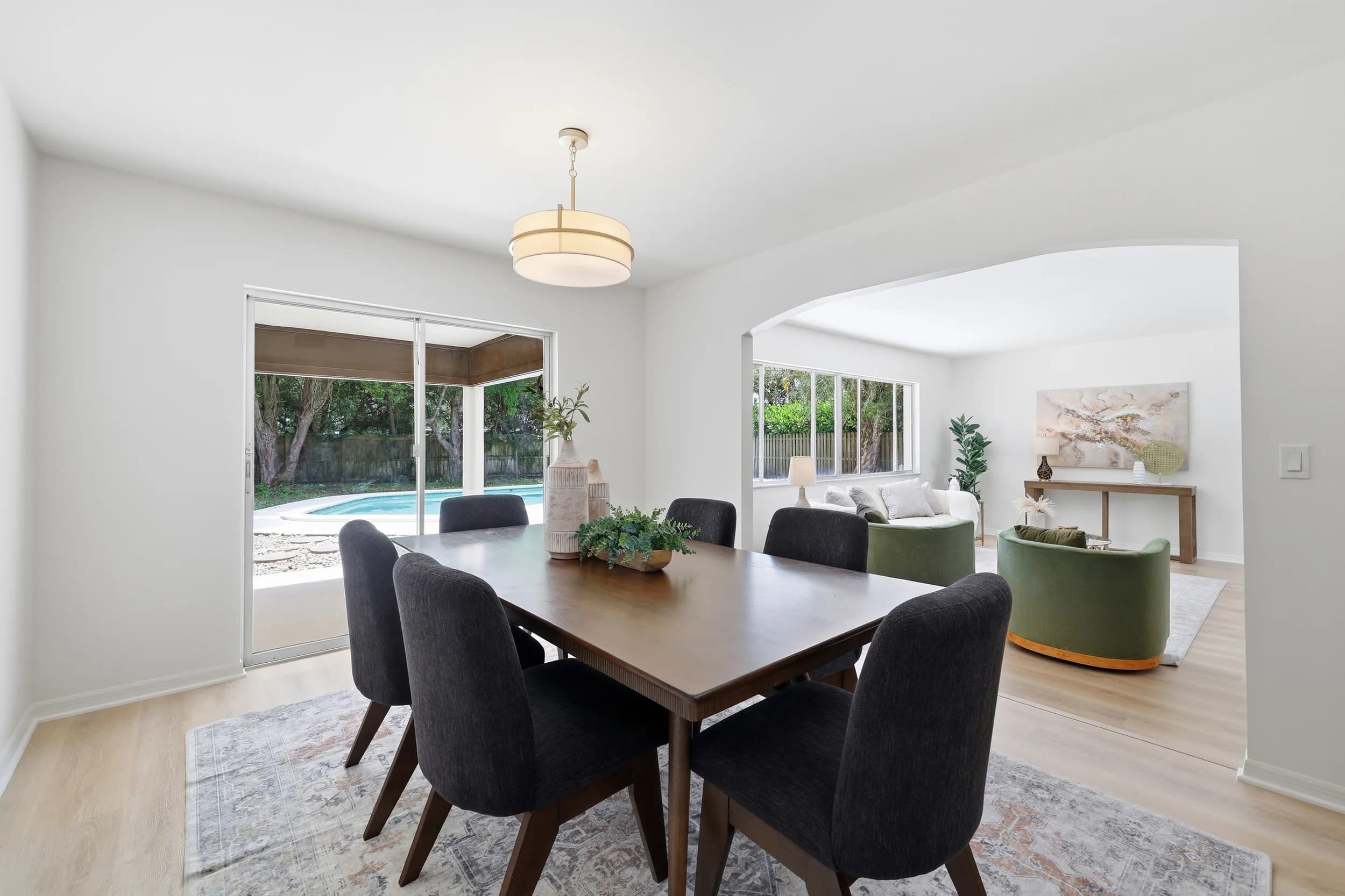 Dining room with dark wood table and charcoal chairs, sliders to the pool, green sofas beyond