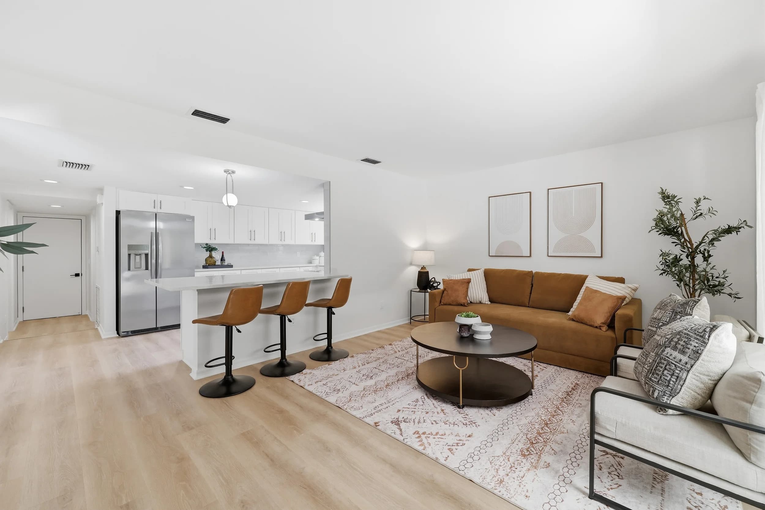 Open-plan living area with cognac sofa and round coffee table beside a white kitchen with bar stools