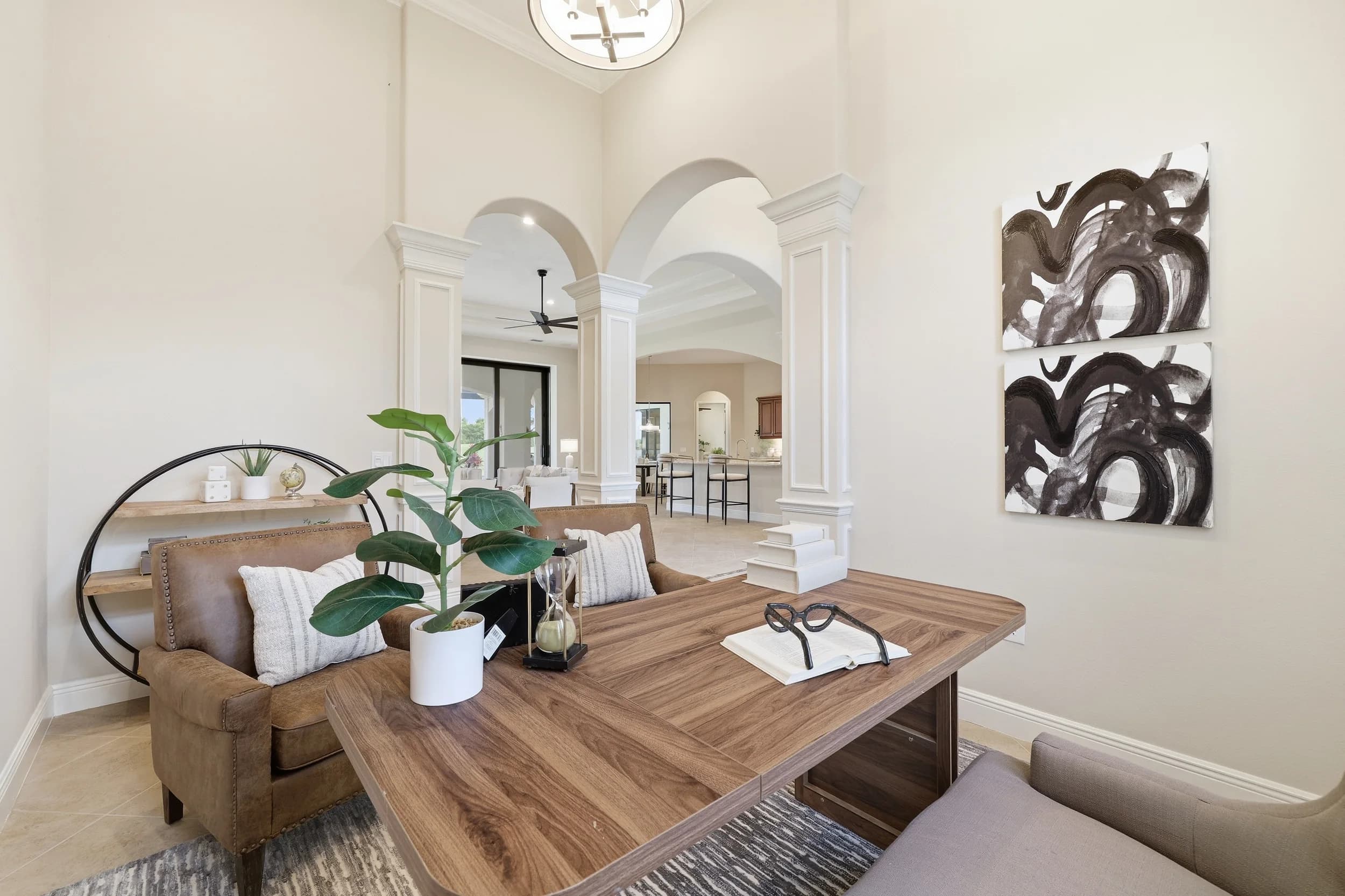 Study staged with walnut desk, leather loveseat and abstract art under arched columns