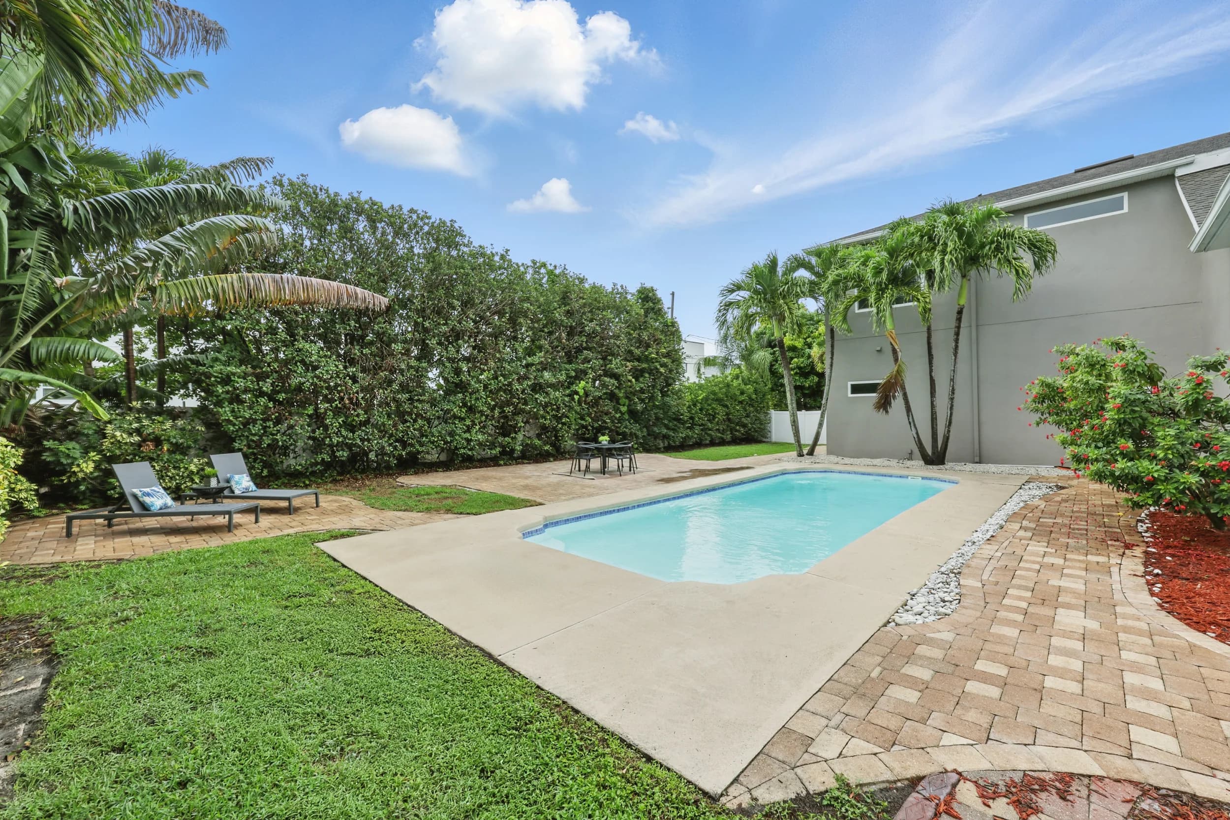 Backyard pool with paver deck, staged lounge chairs and dining set framed by palms