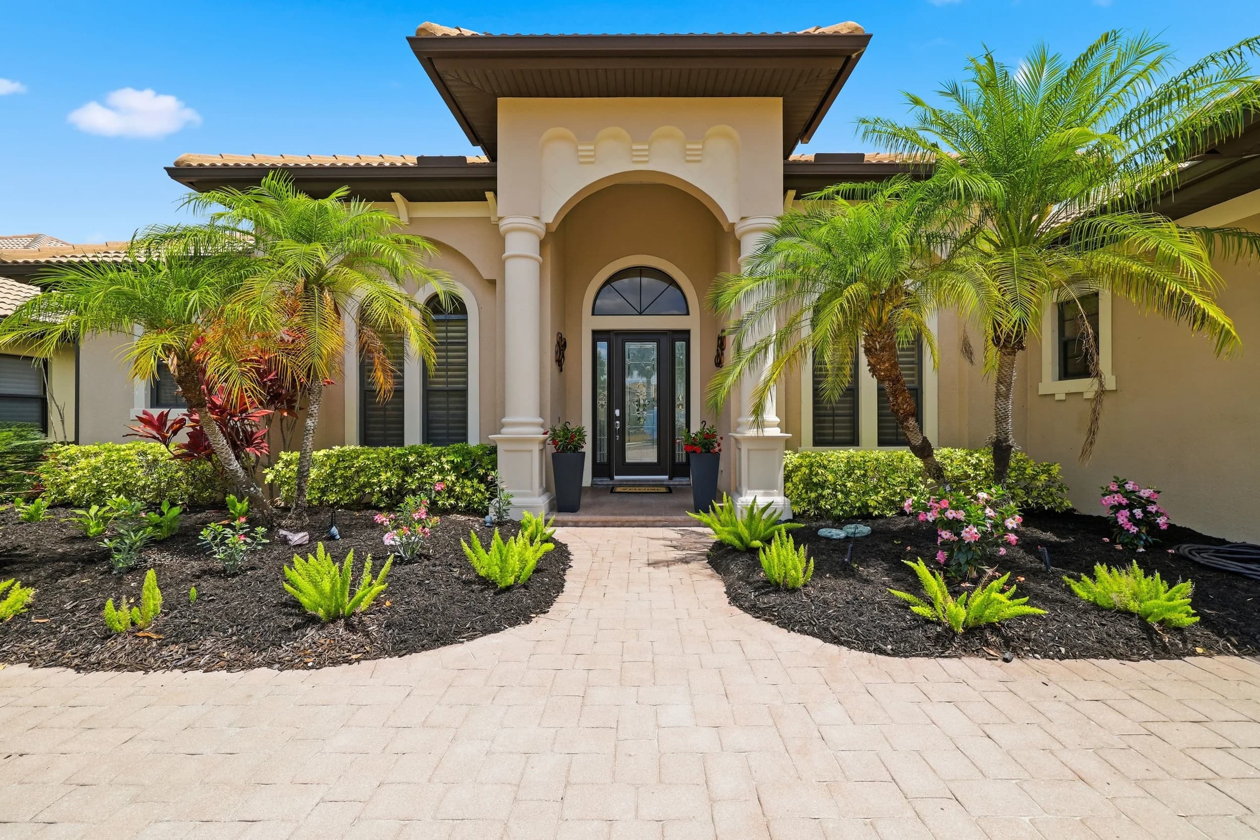 Mediterranean-style entry with arched portico, columns, potted flowers and palms