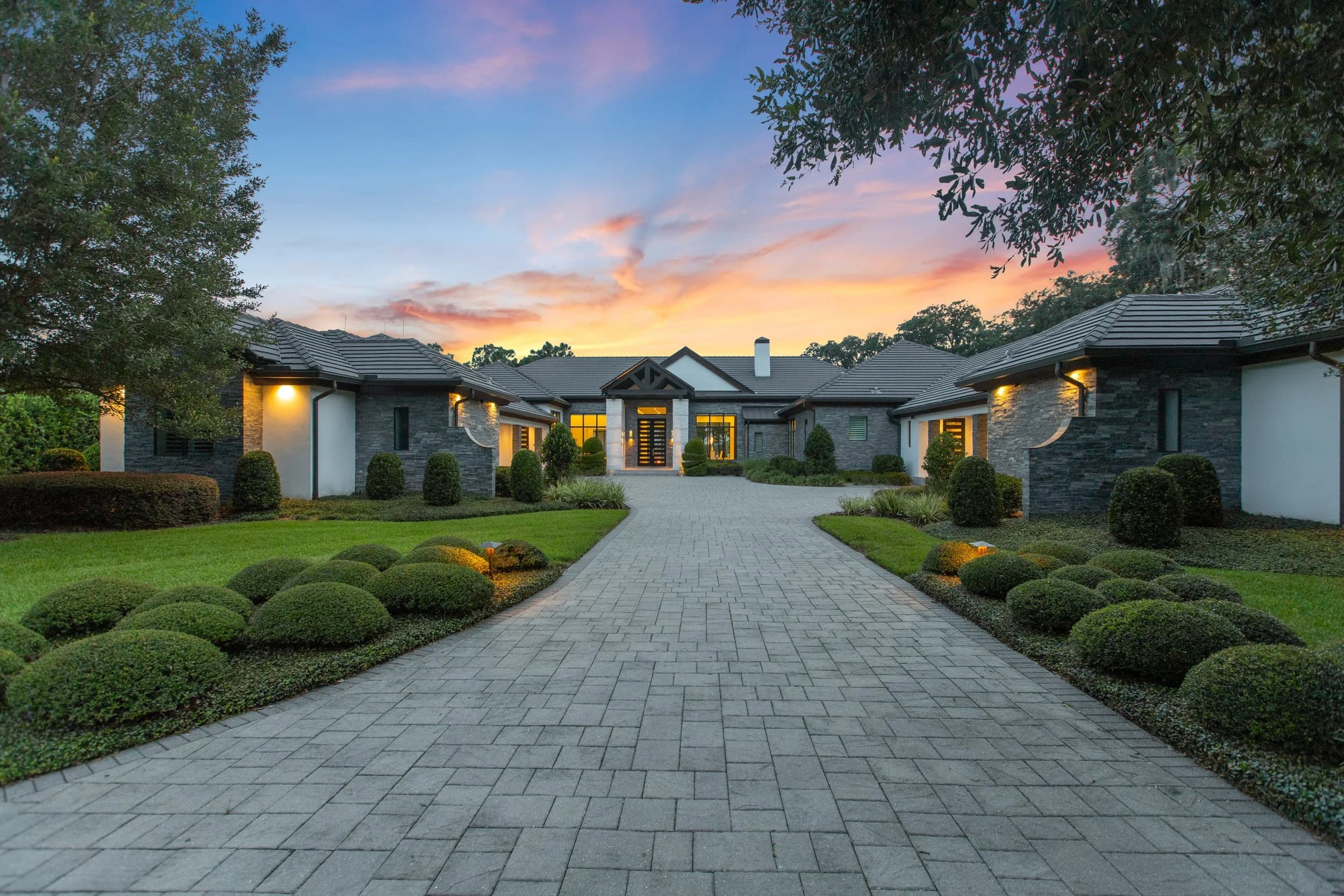 Single-story luxury home at twilight with lit landscaping and paver drive