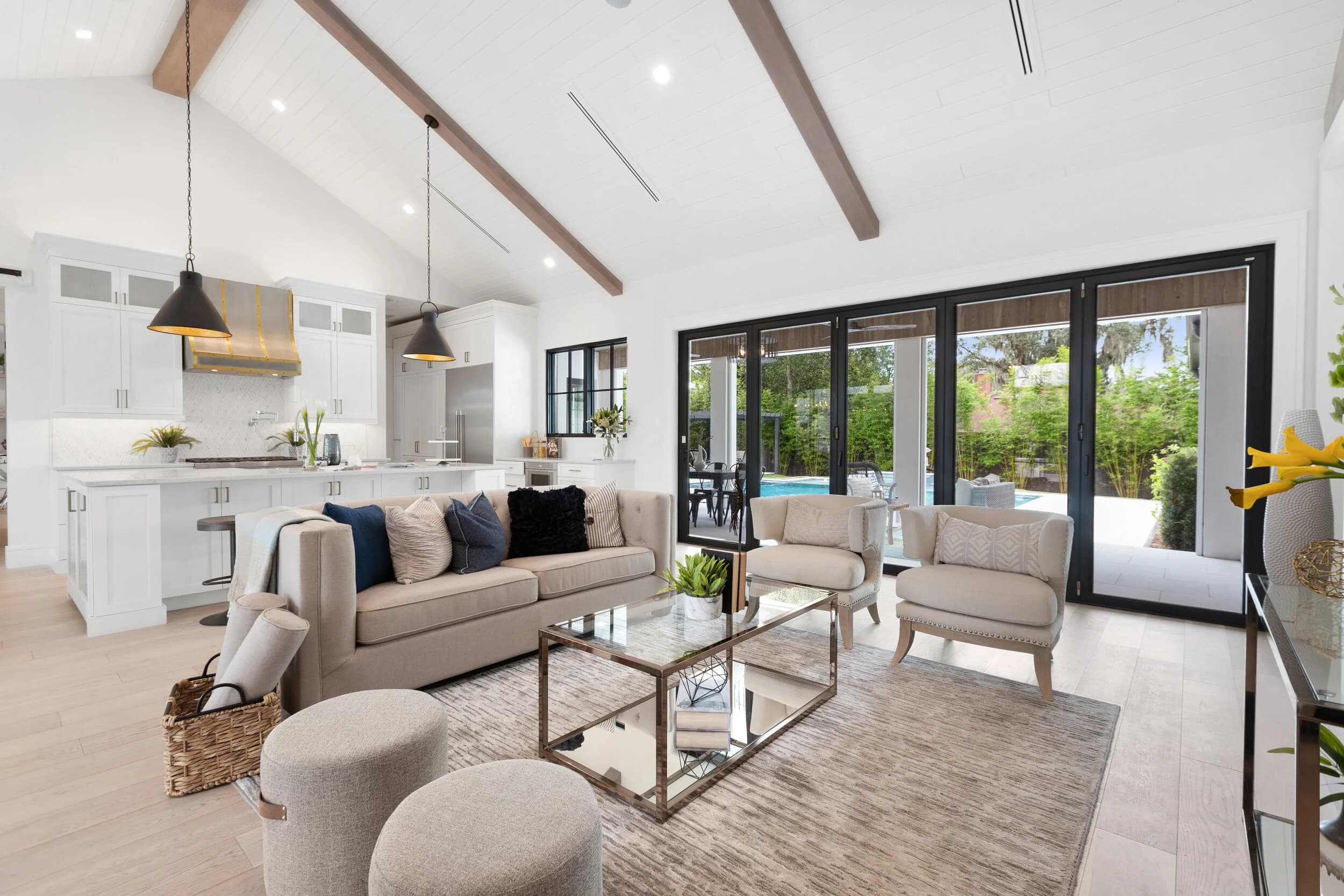 Vaulted great room with beams, sofas, and glass doors to the pool