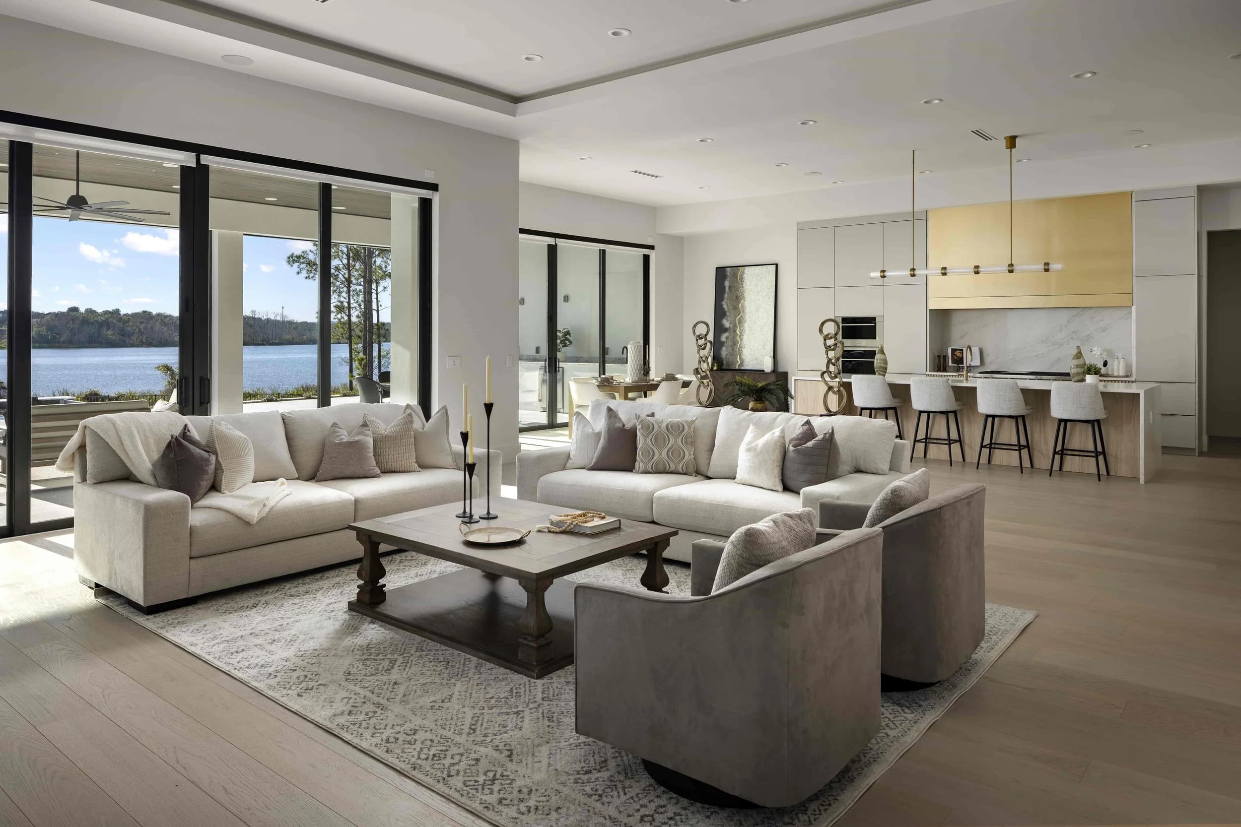 Living room with sofas and a kitchen beyond, glass doors to the lake