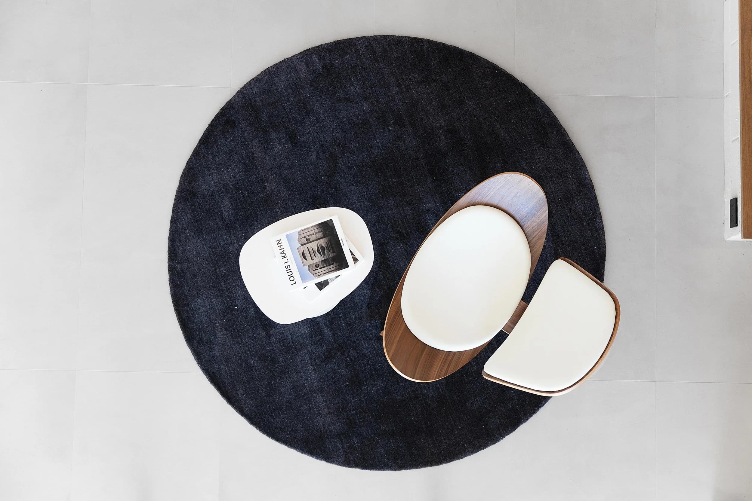 Top-down detail of a round black rug, cream armchair, and coffee table styling