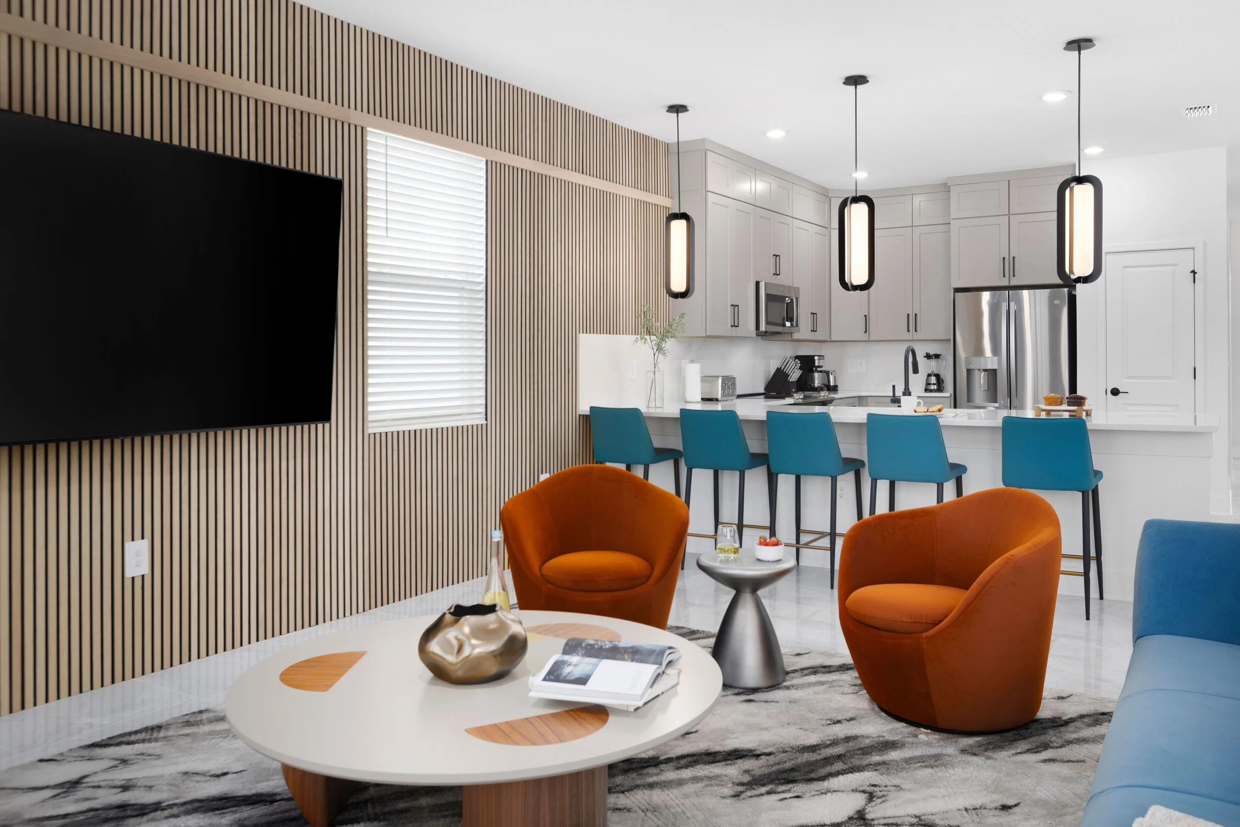 Living room with orange armchairs, slatted media wall, and blue counter stools