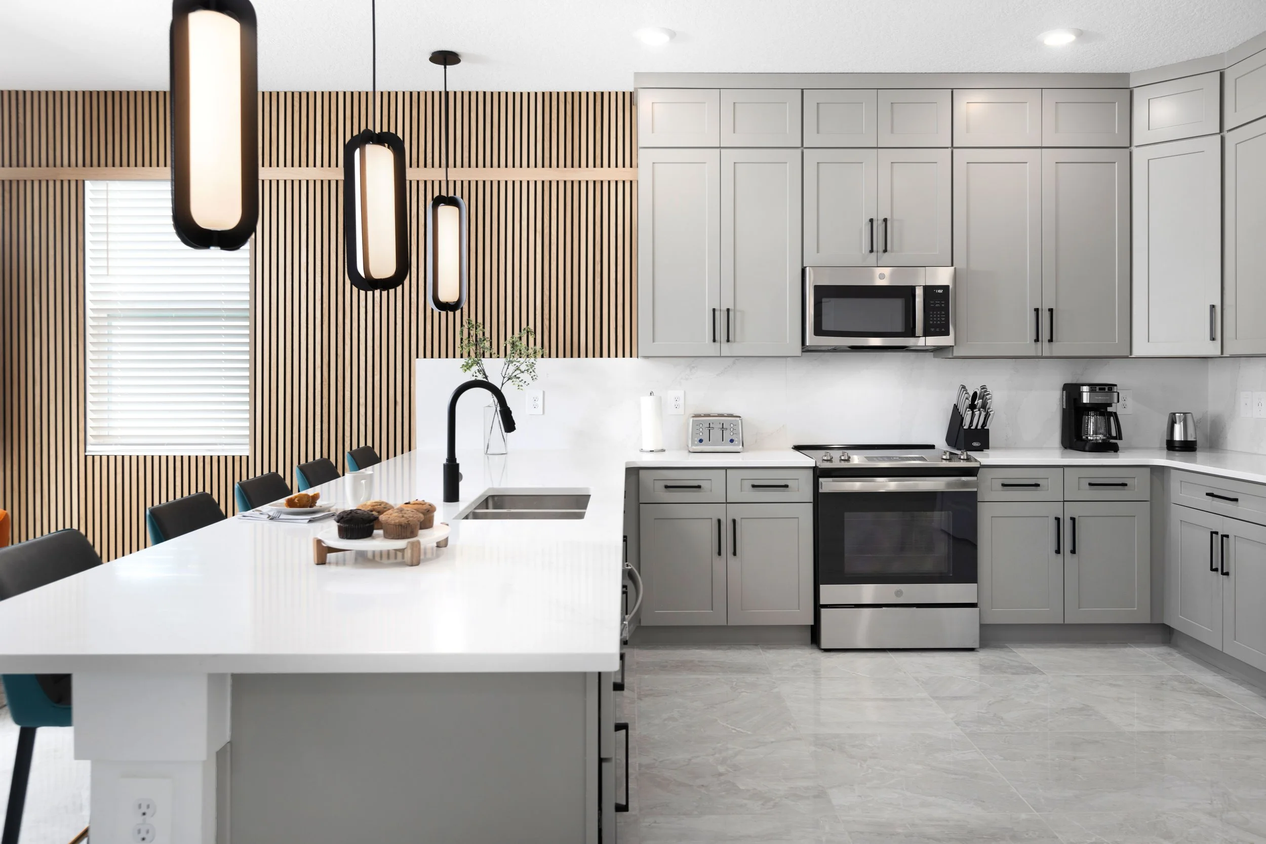 Kitchen with white cabinets, vertical wood slat wall, and black pendants