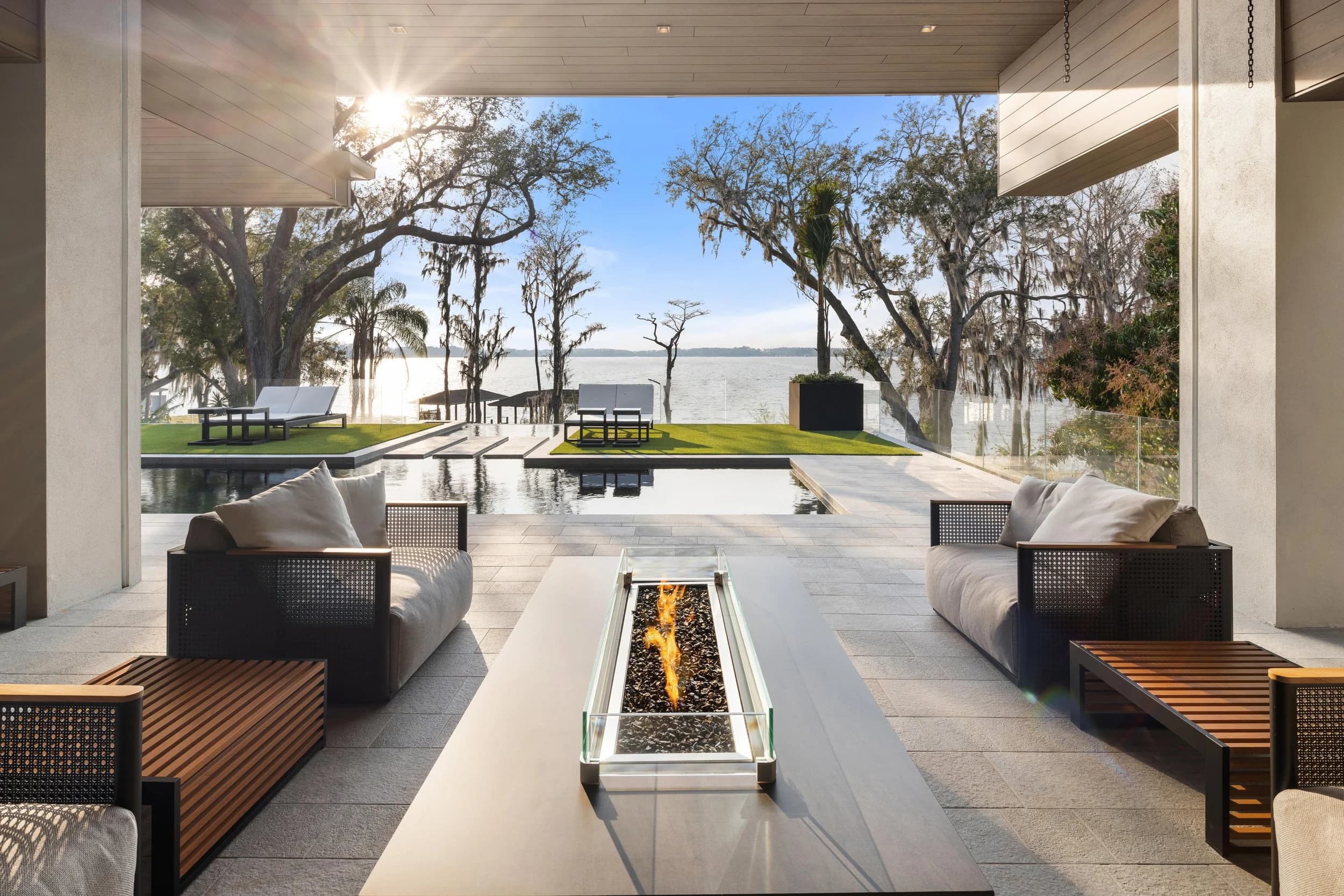 Covered lanai with a linear fire feature, outdoor sofa, and lake view at blue hour