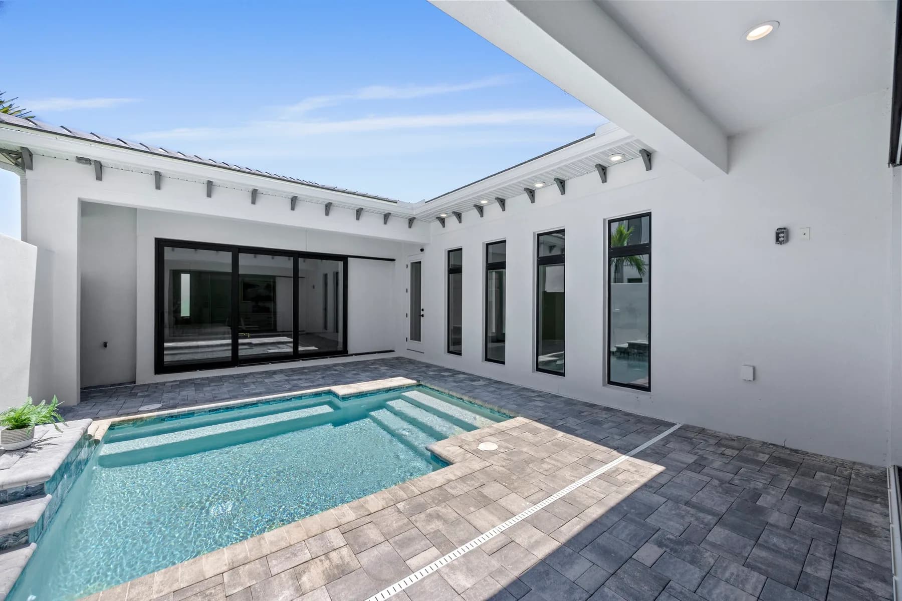 Modern courtyard with a swimming pool surrounded by a U-shaped residential building, under a clear blue sky.