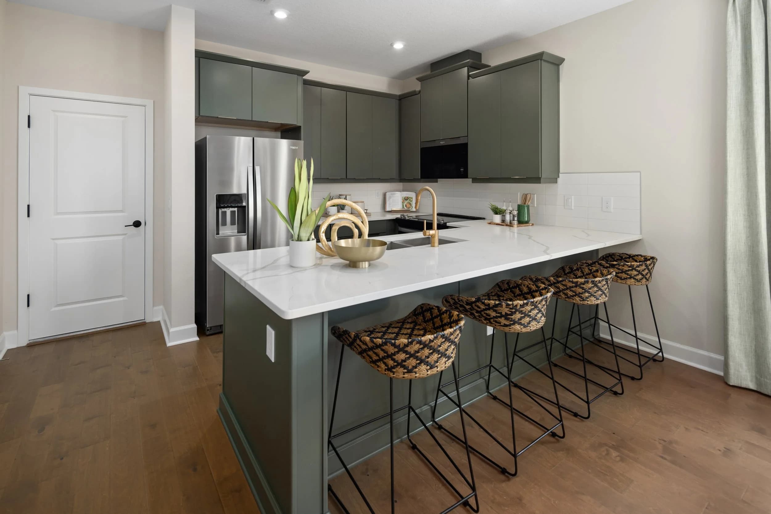 Kitchen with sage green cabinets, white quartz island, rattan stools and brass faucet