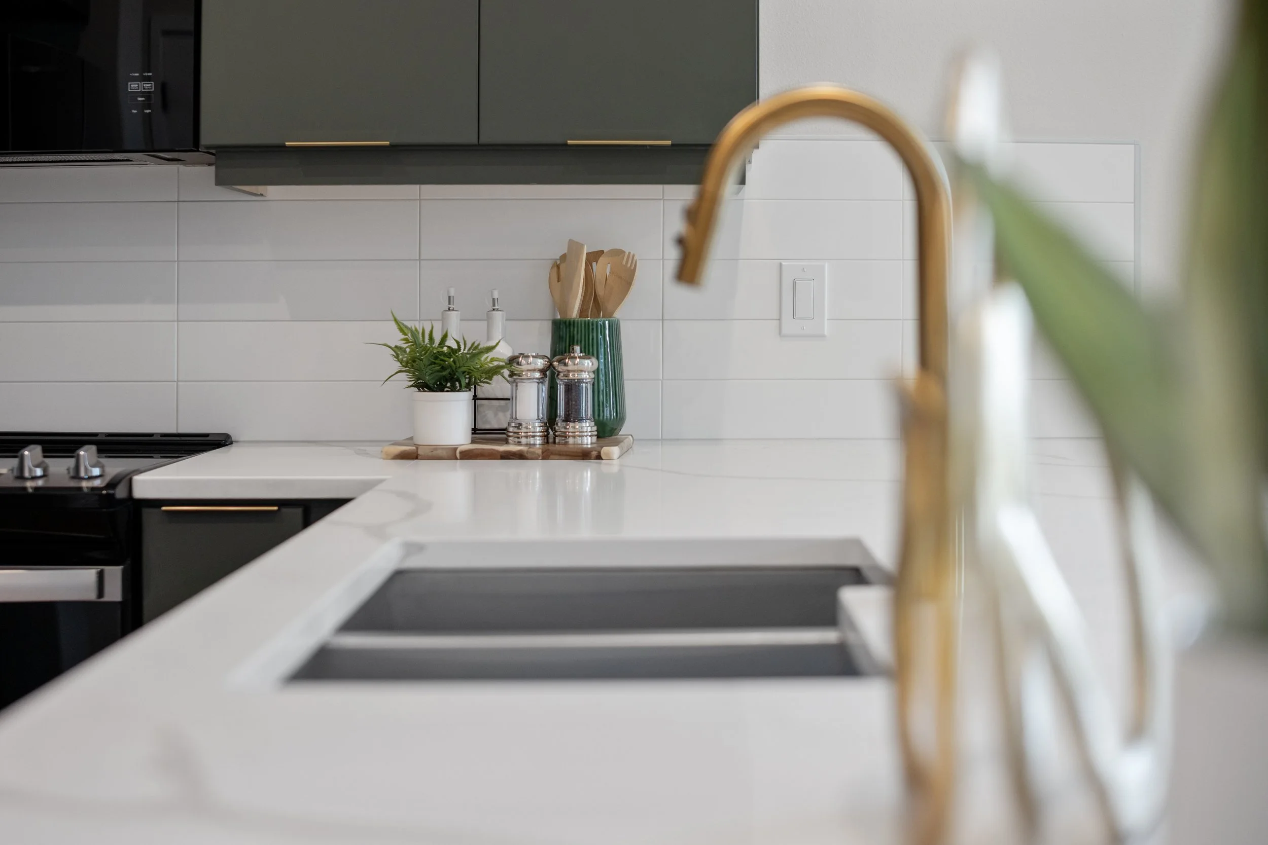 Close detail of the brass kitchen faucet, quartz sink and white tile backsplash
