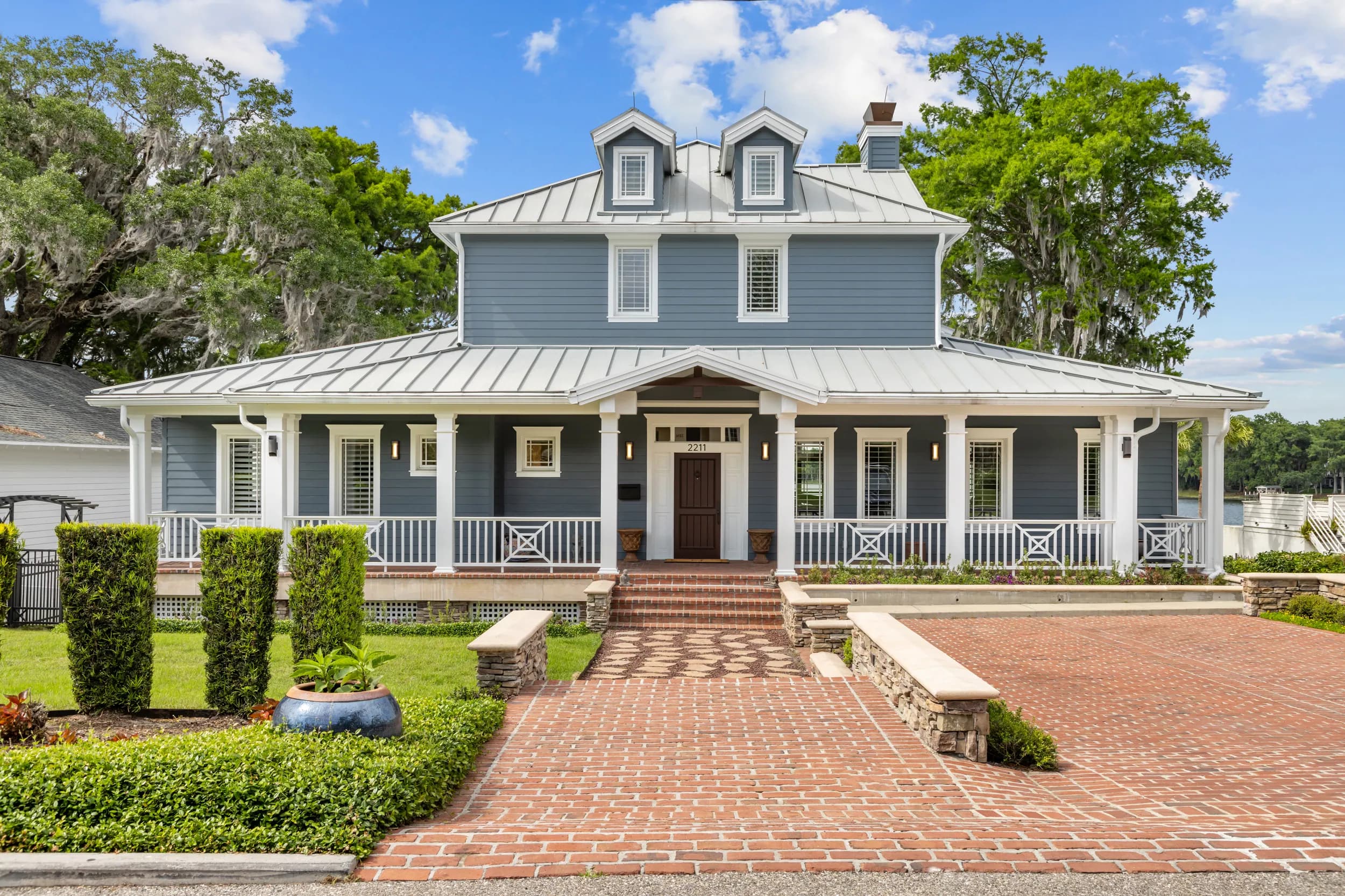 Blue Lowcountry home with standing-seam roof, wraparound porch and brick drive