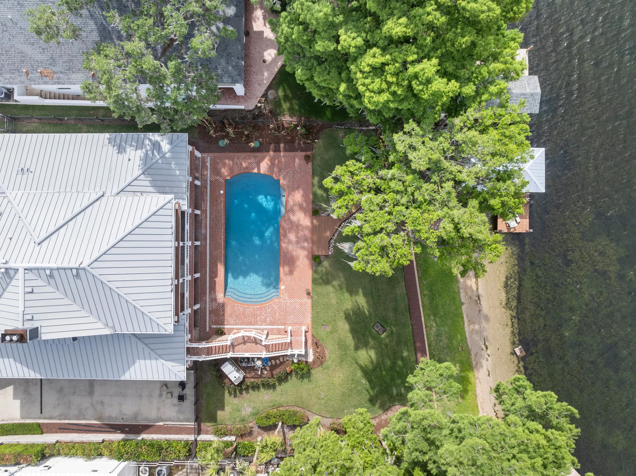 Top-down aerial of the metal roof, pool and dock on the lake