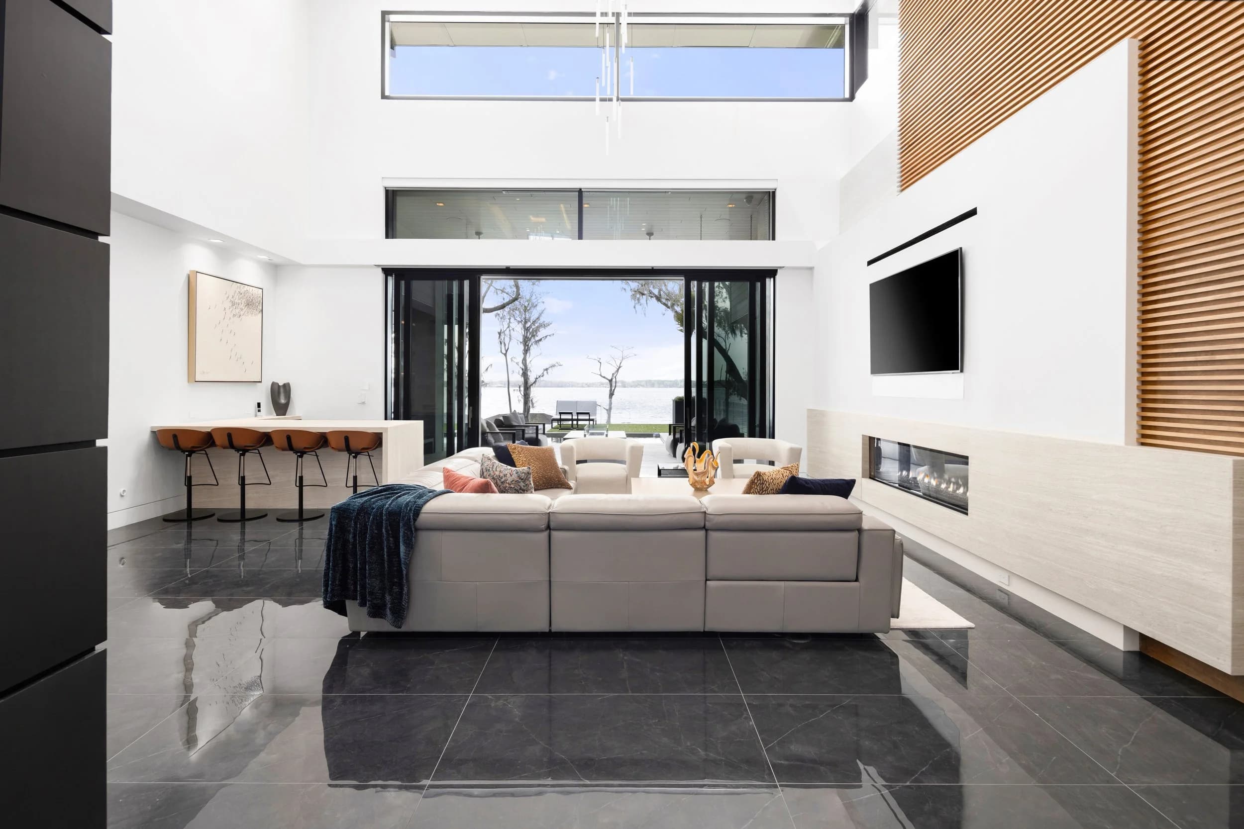 Two-story great room with sectional, linear fireplace and sliding glass wall opening to the lake
