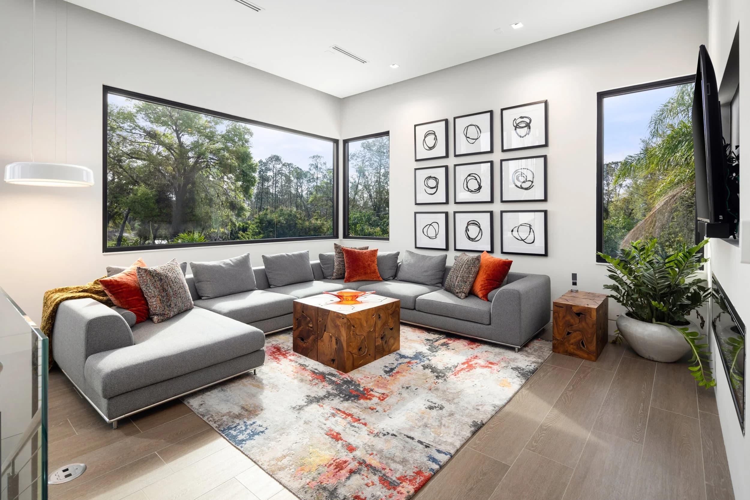 Lounge with gray sectional, wood cube table, grid of nine framed prints and tree views