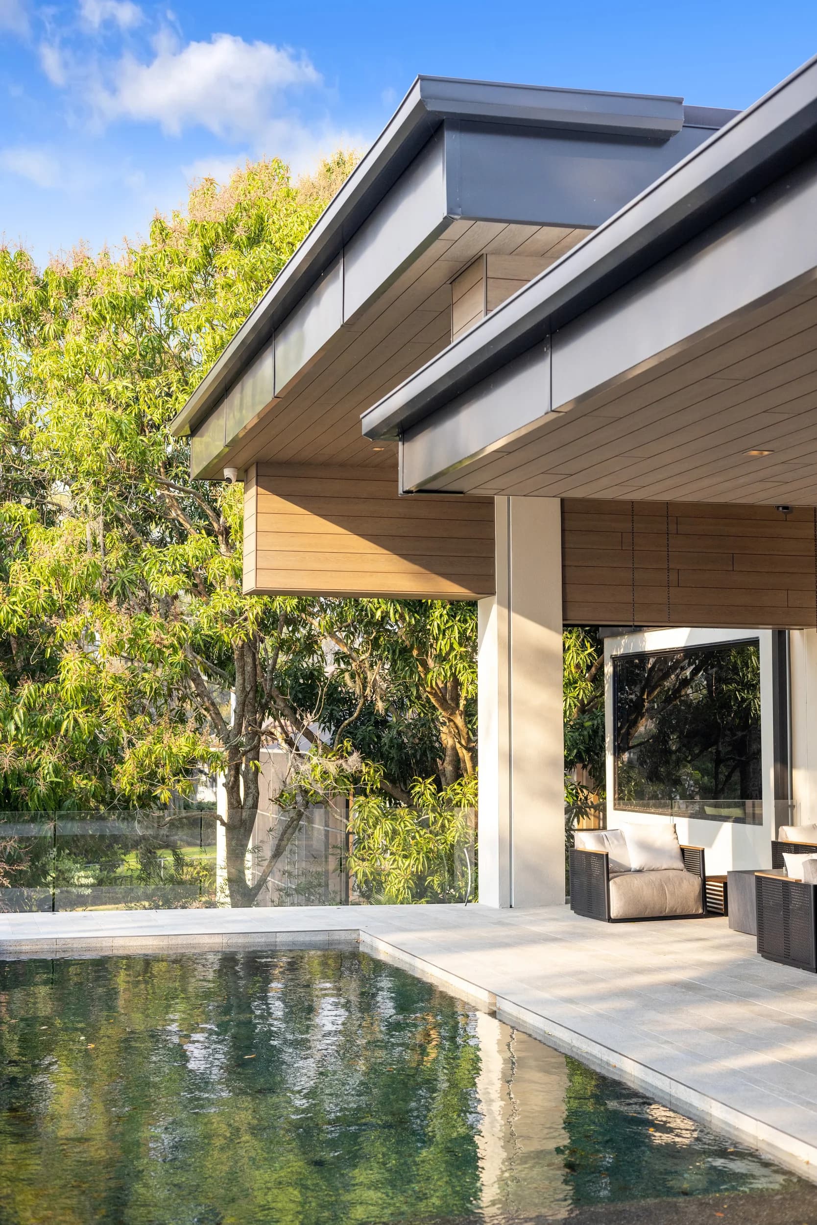 Vertical view of the pool corner under the cantilevered roof with oak trees behind