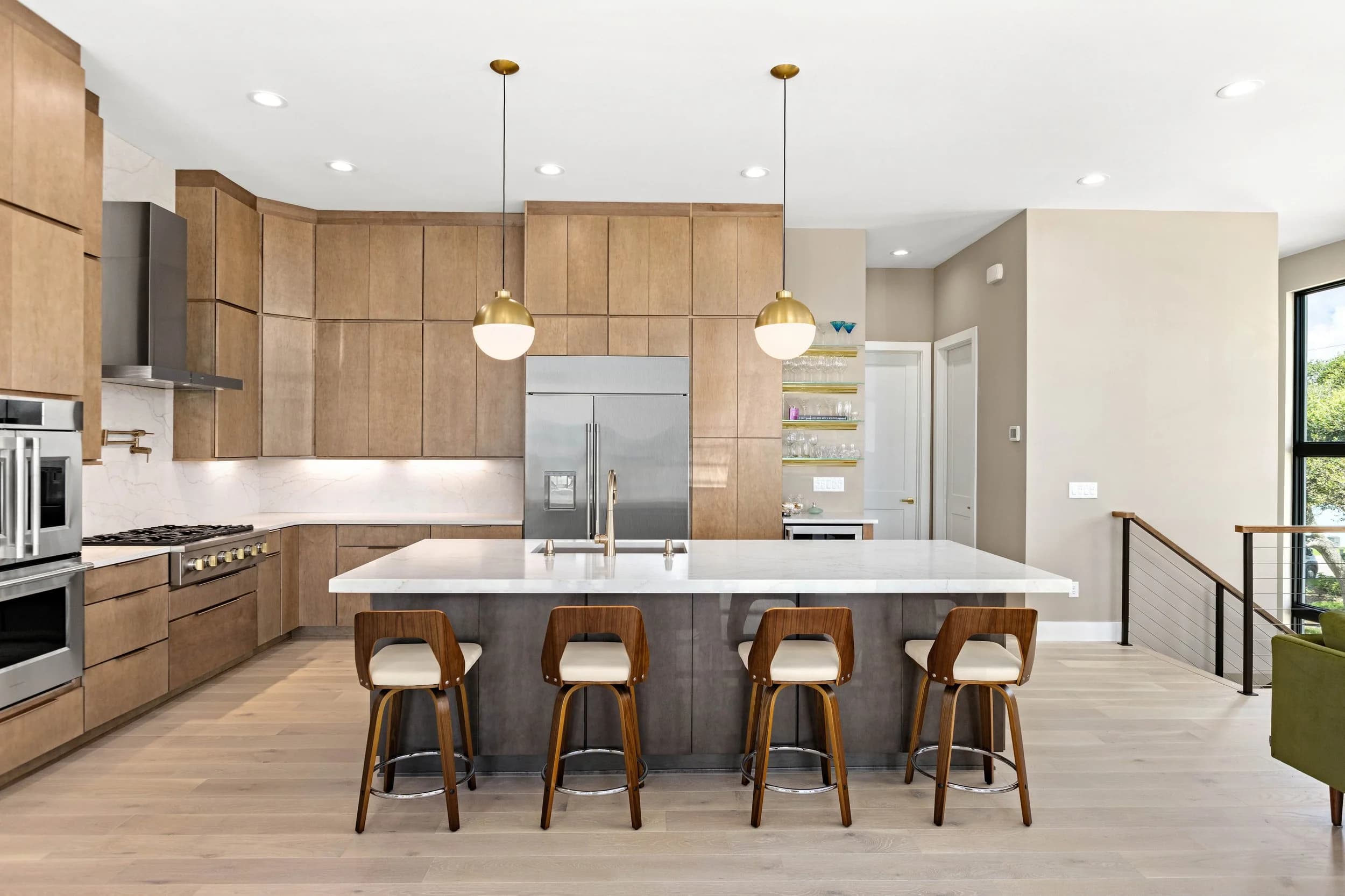 Kitchen with light wood cabinets, white quartz island, walnut stools and brass pendants
