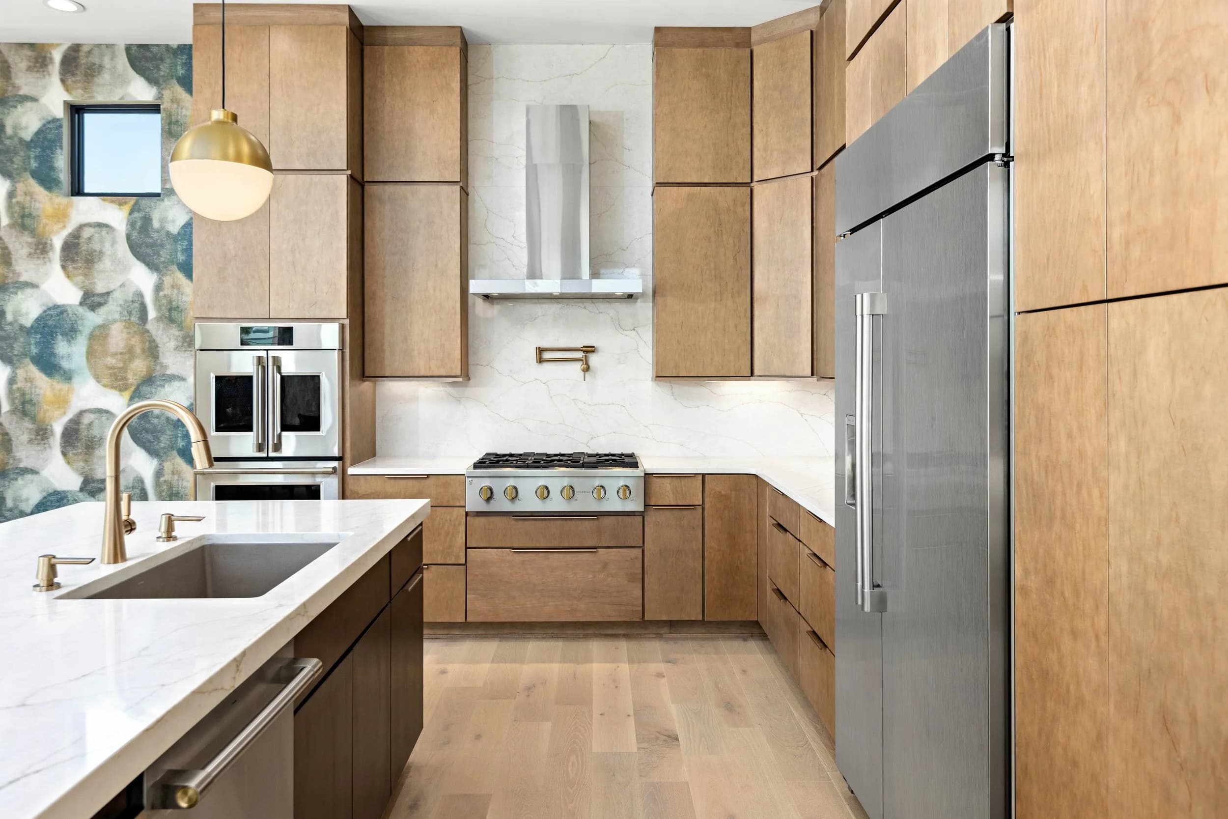 Kitchen range wall with stainless hood, gas cooktop, marble backsplash and patterned wallpaper