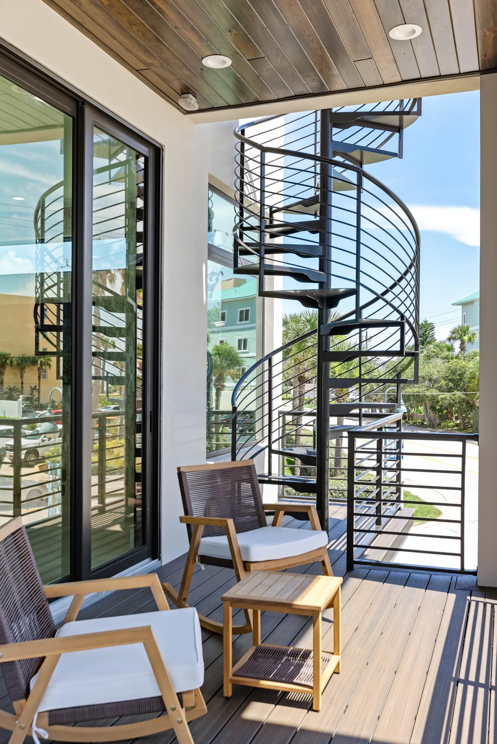 Vertical view of the covered balcony with teak chairs and the black exterior spiral stair