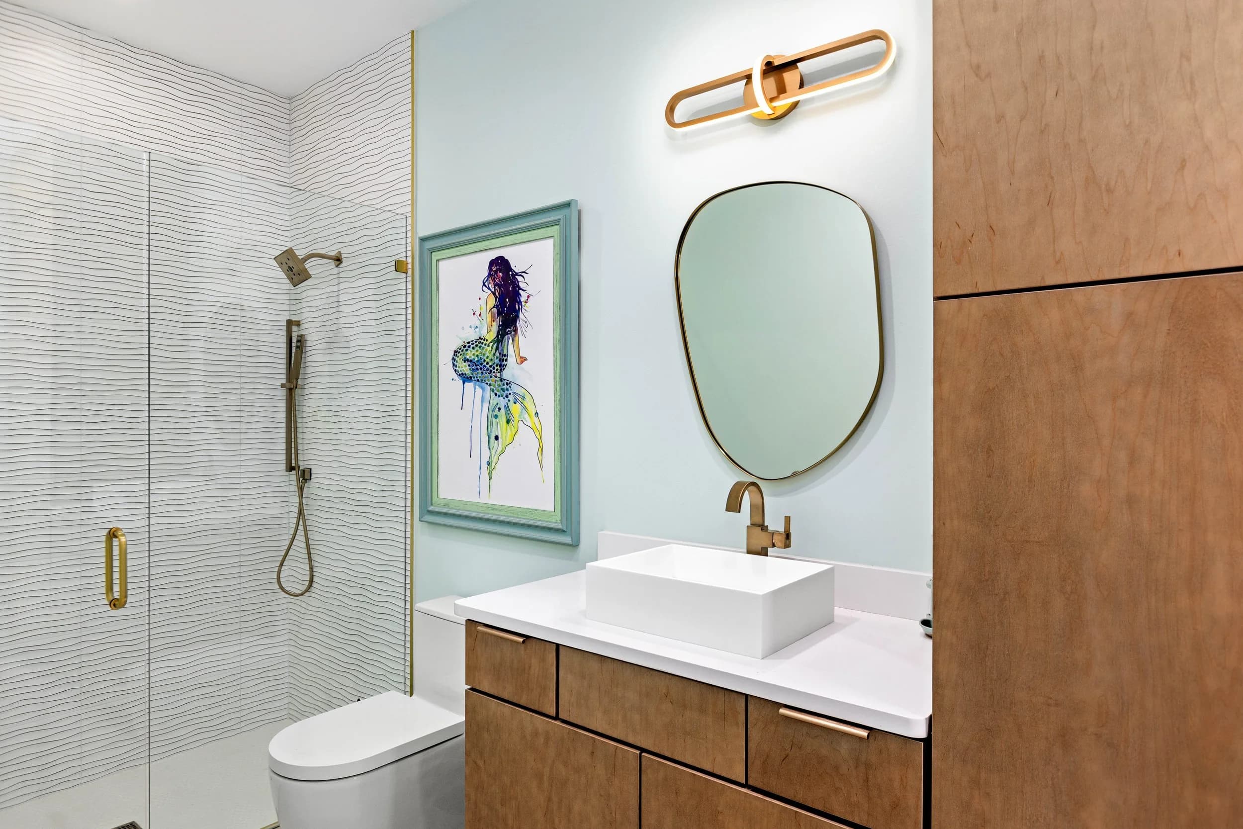 Guest bath with glass shower, vessel sink, brass fixtures and mermaid art