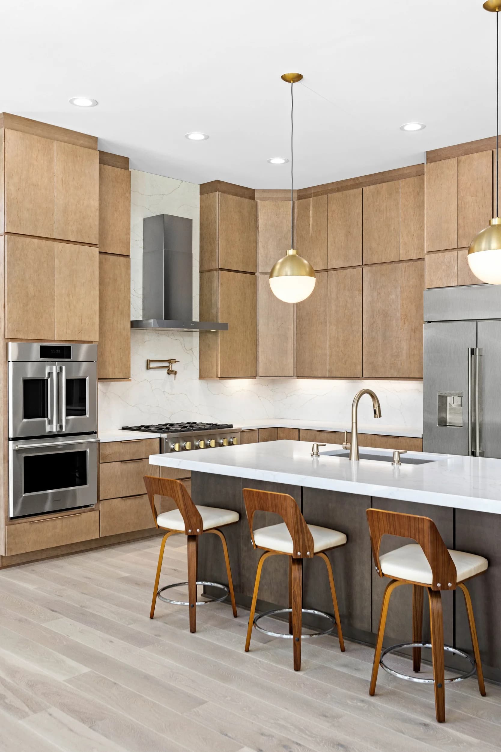 Vertical view of the kitchen island with walnut stools and brass pendants