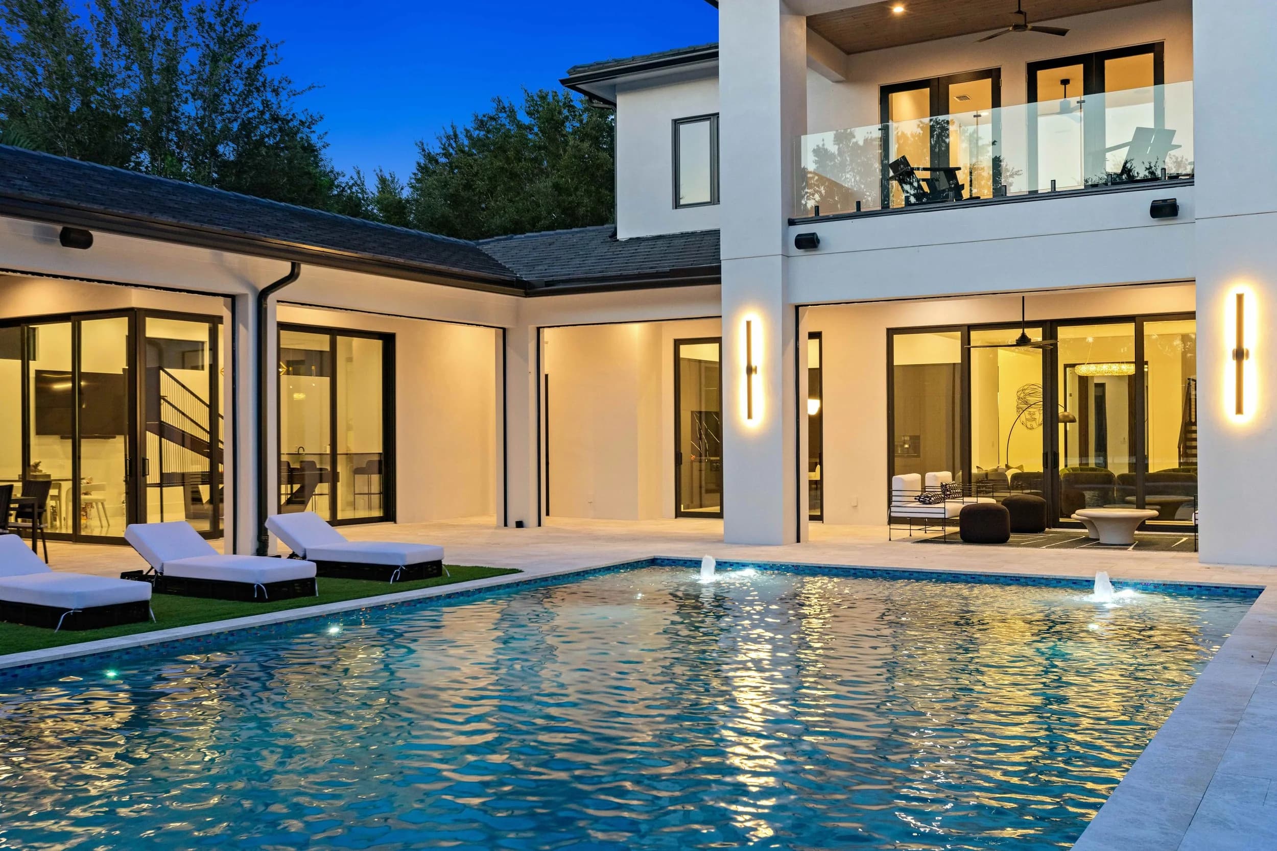 Rear elevation at twilight with lit interiors, balcony and pool in the foreground