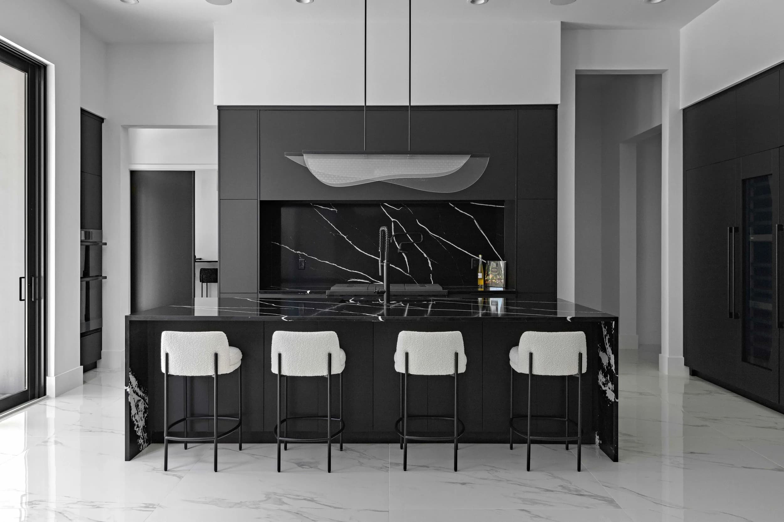 Monochrome kitchen with black marble island, four white stools and white porcelain floor