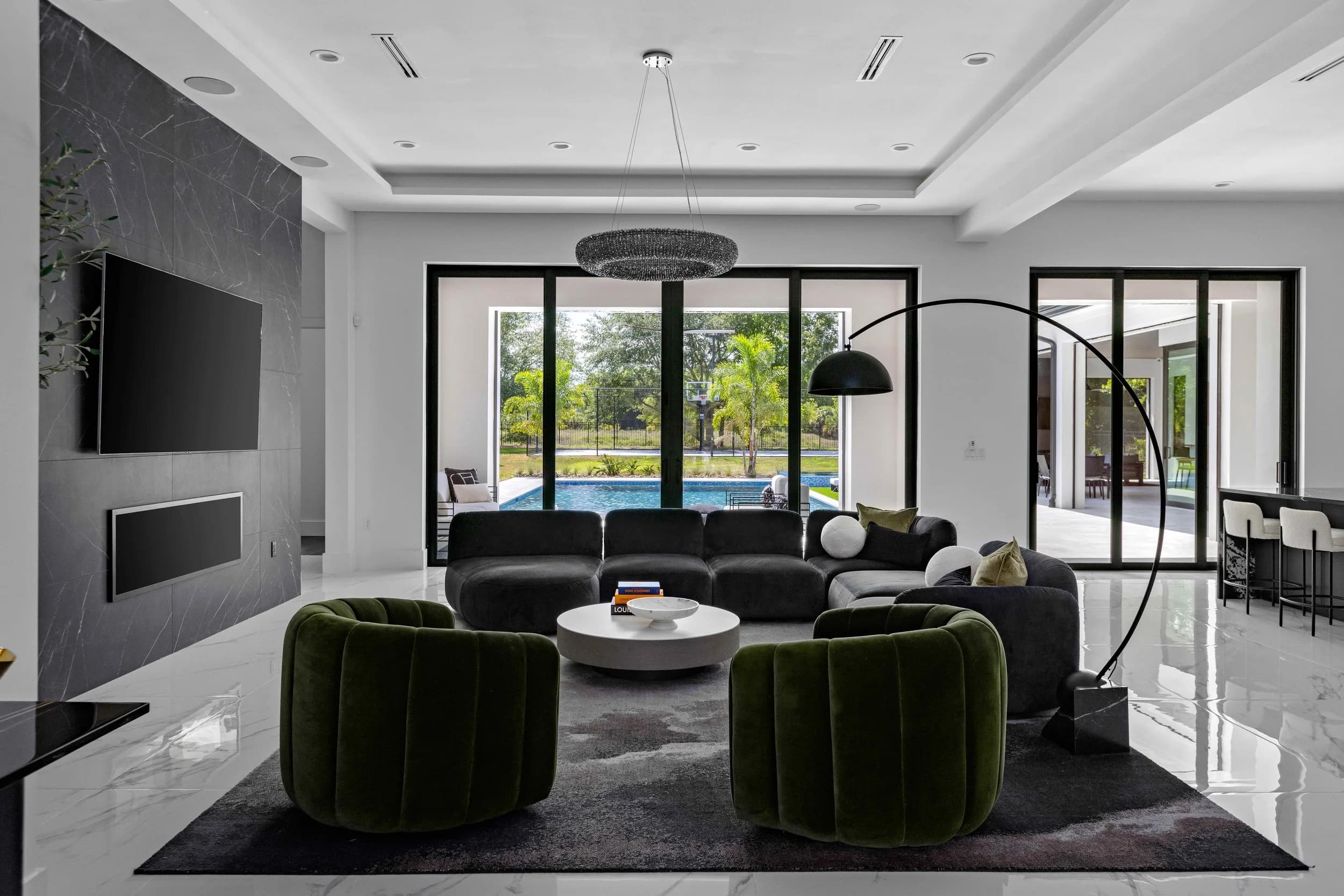 Great room with green velvet chairs, black sectional, stone TV wall and sliders to the pool