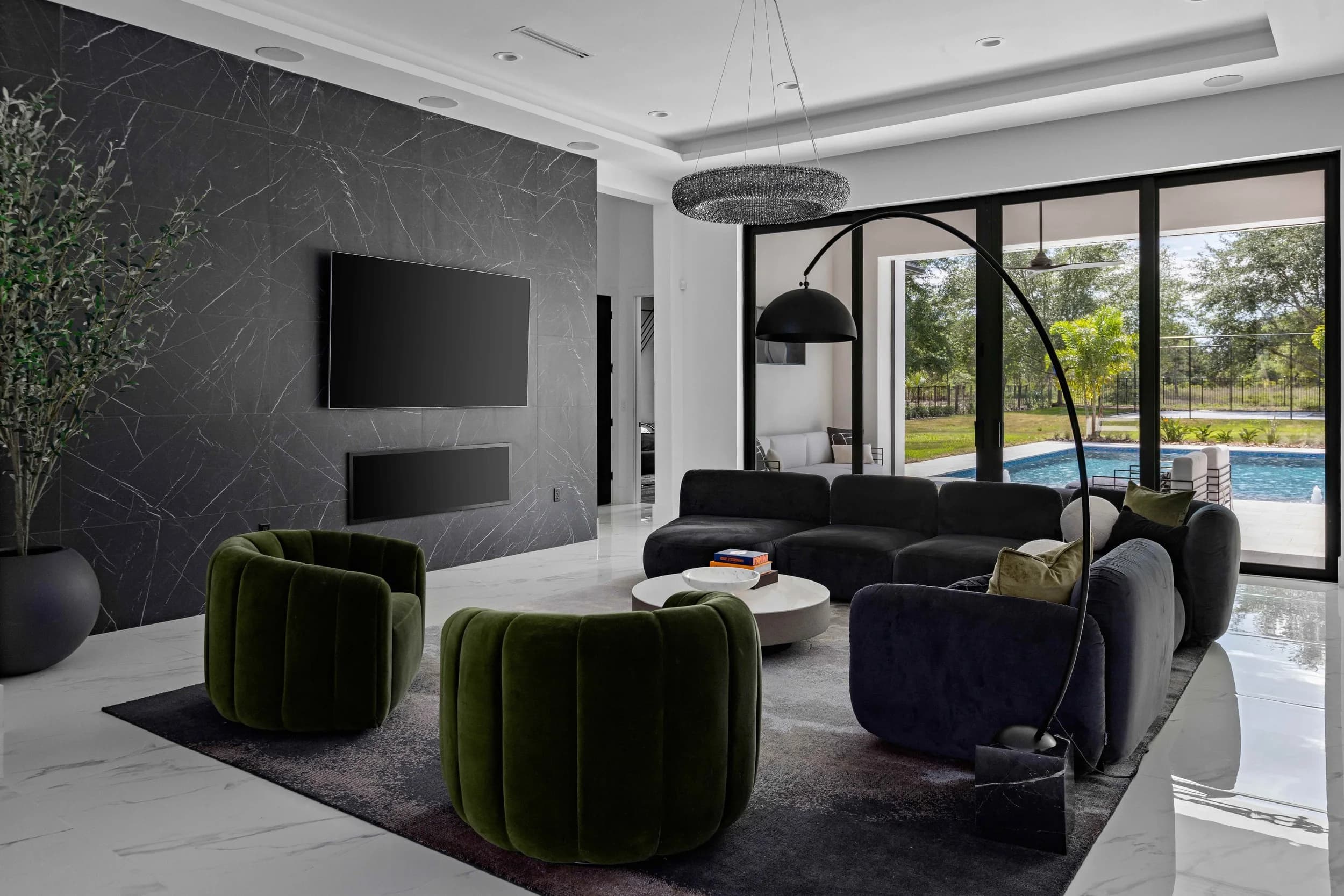 Great room with dark stone feature wall, arc floor lamp, olive tree and pool view