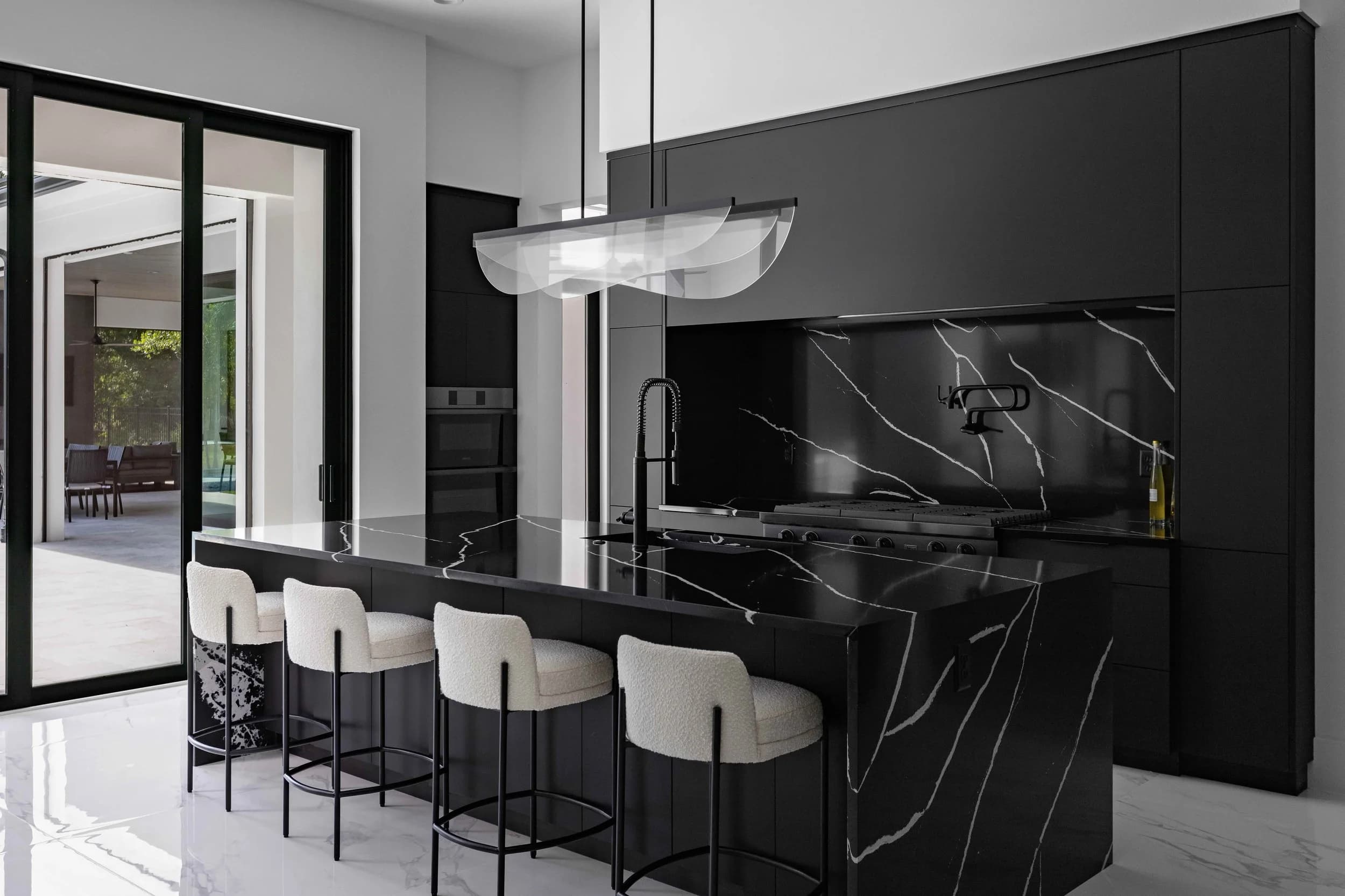 Black marble kitchen island with white stools and sliding doors open to the lanai