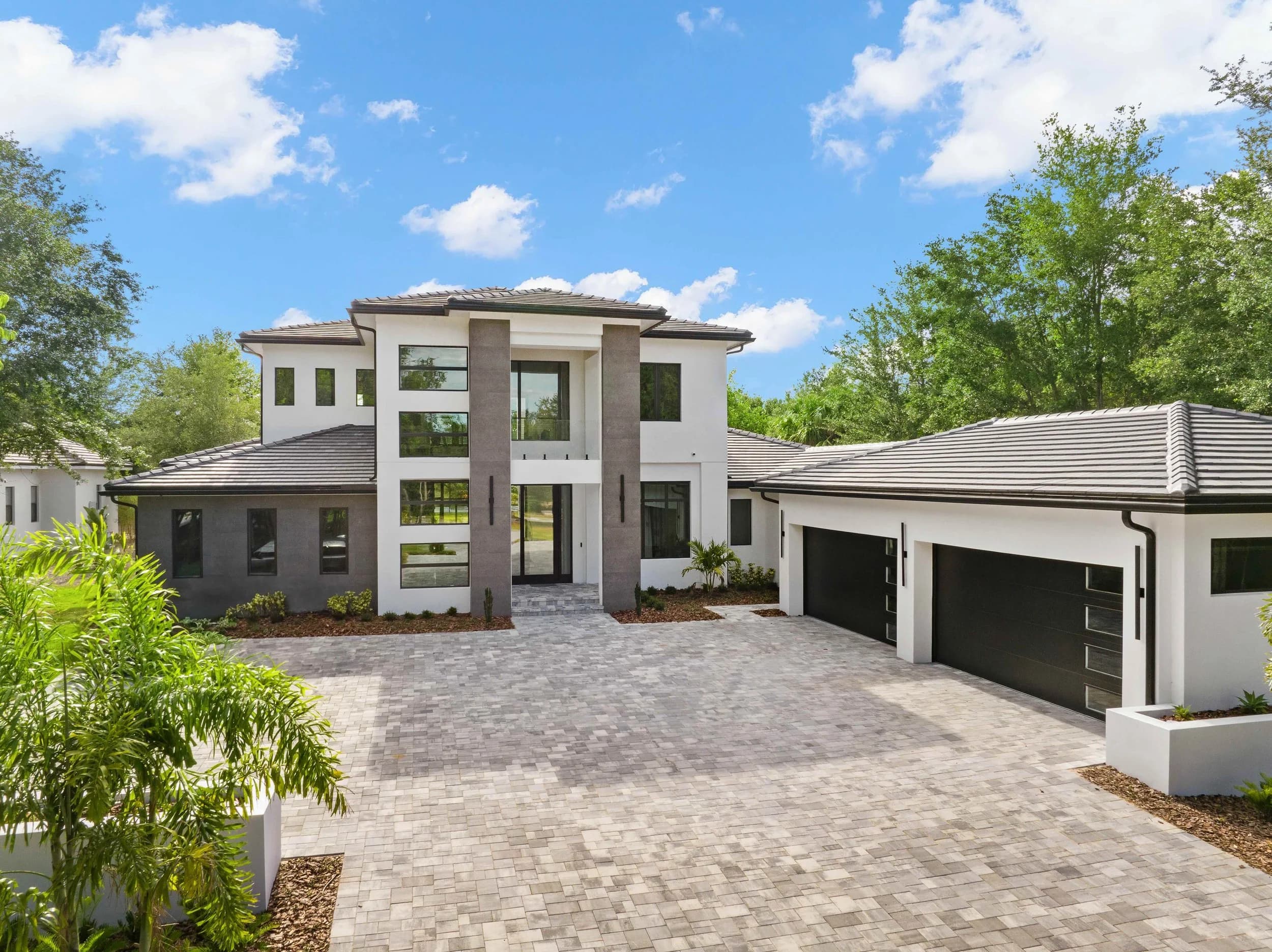 Front elevation by day with paver driveway, black garage doors and blue sky