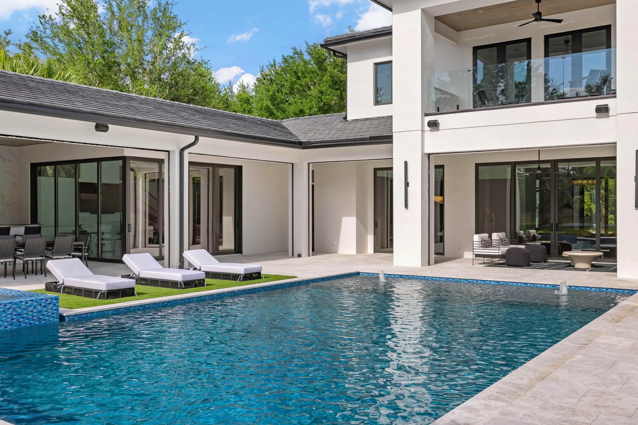 Rear elevation by day with L-shaped house, pool and loungers on turf