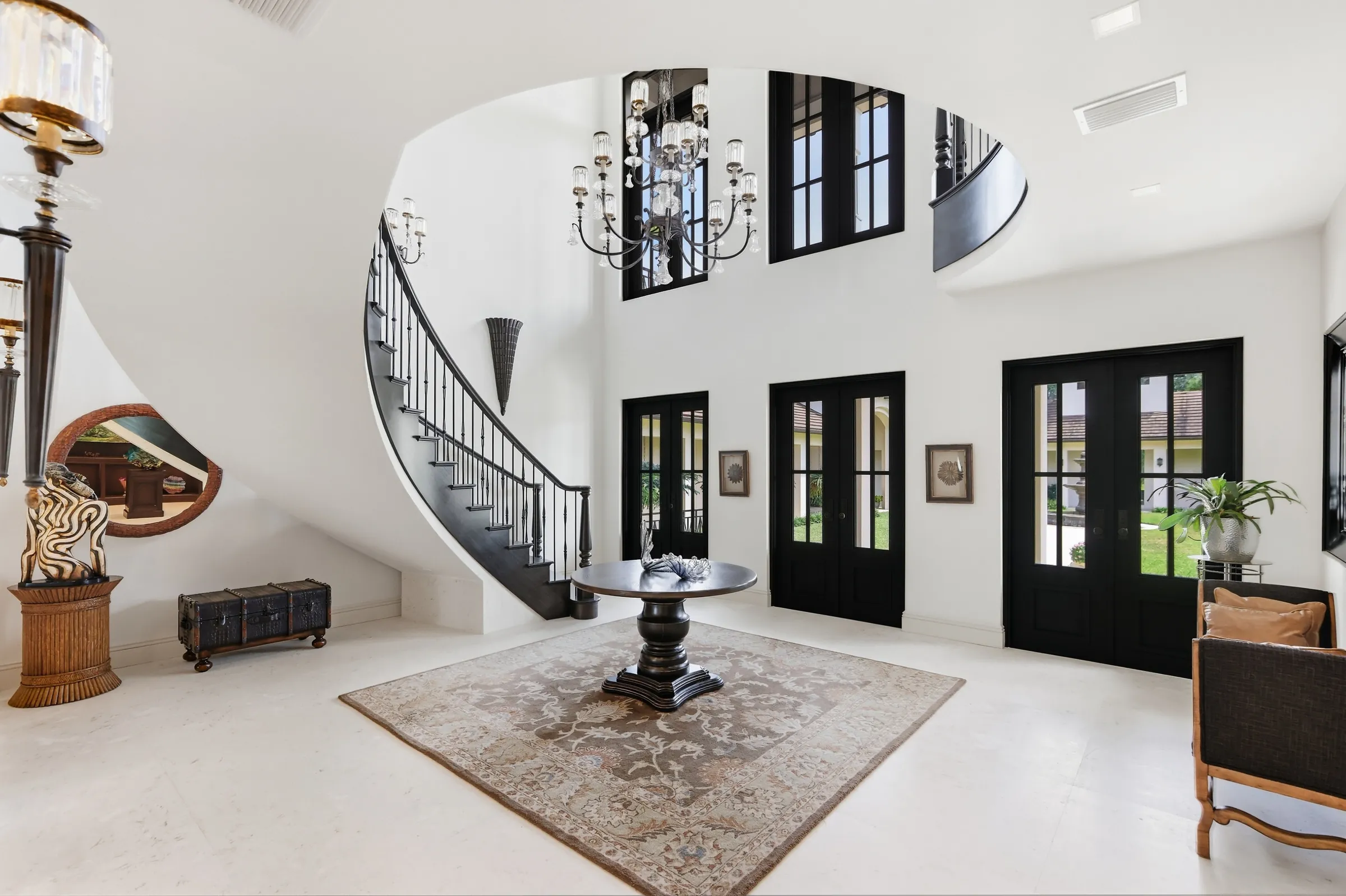 Two-story foyer with a curved staircase, iron chandelier and limestone floor